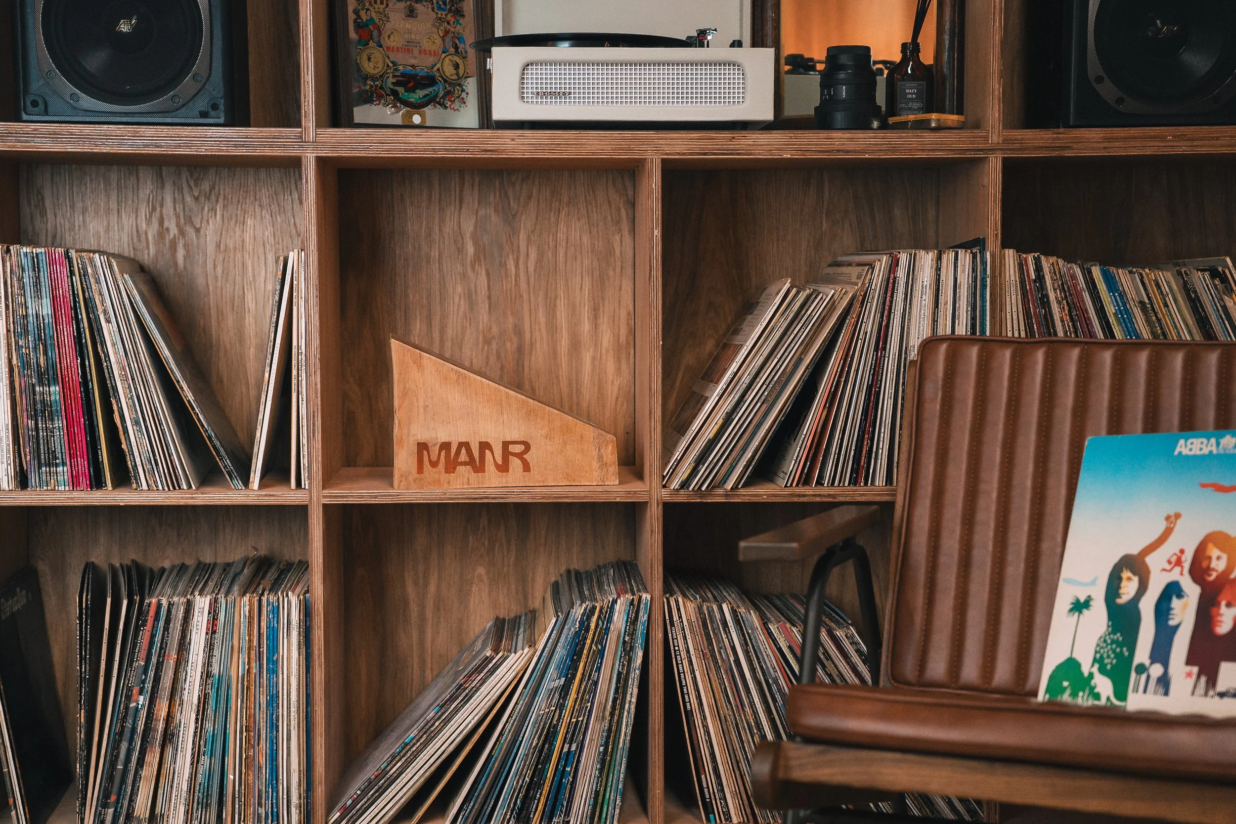 A wooden shelving unit filled with vinyl records, a stereo system on top, and a vintage pizza box.