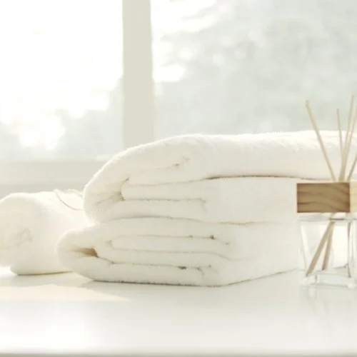 Stack of white towels on a white surface near a window with diffused sunlight.