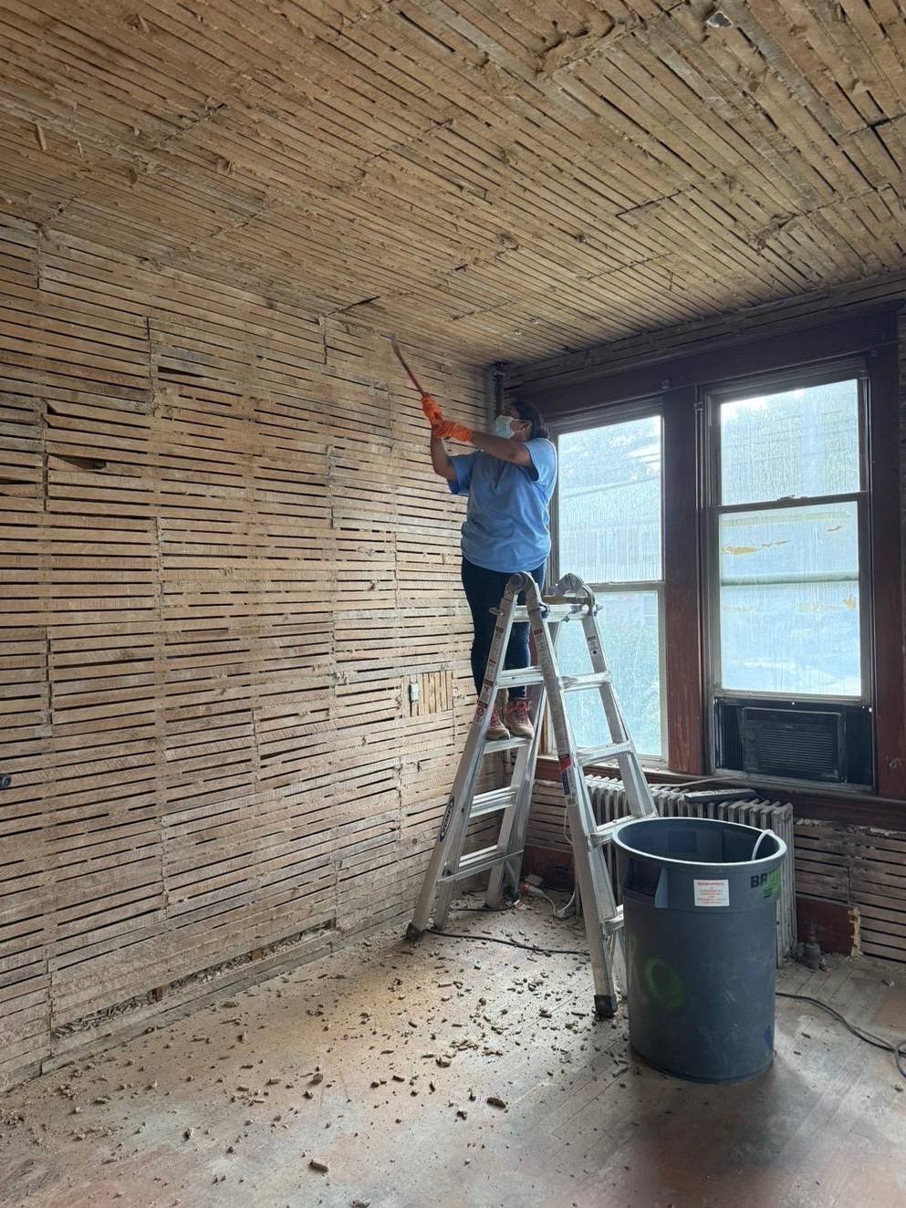 Crew member scraping plaster from a lath ceiling on a ladder
