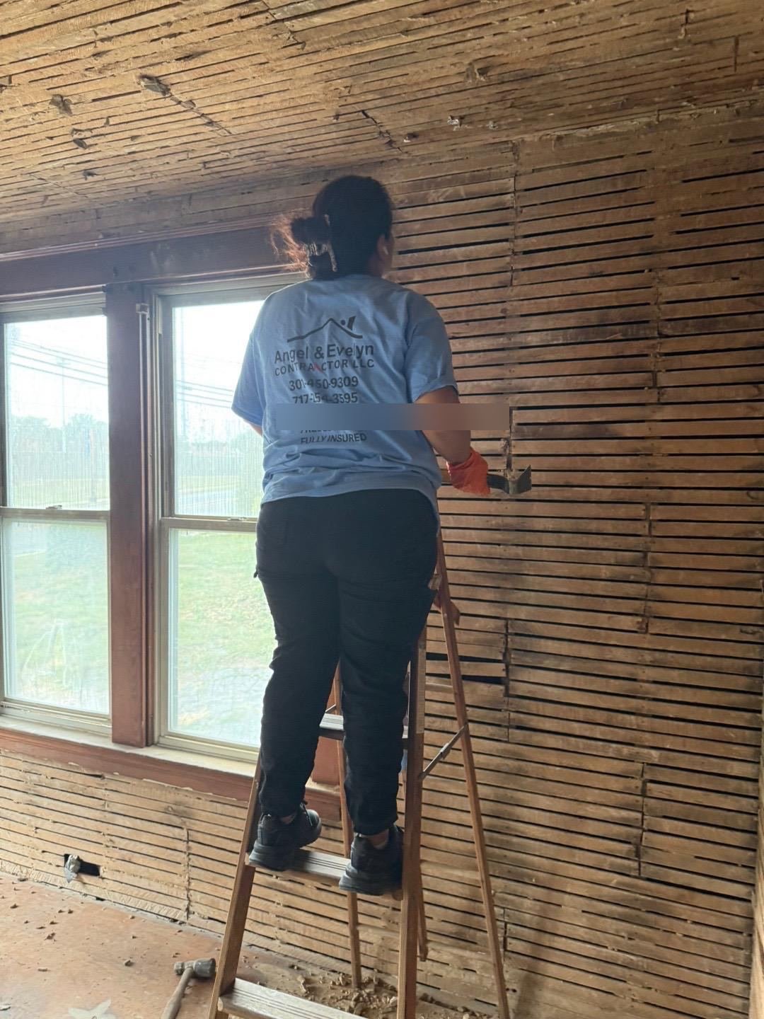 Crew member scraping plaster from interior lath walls