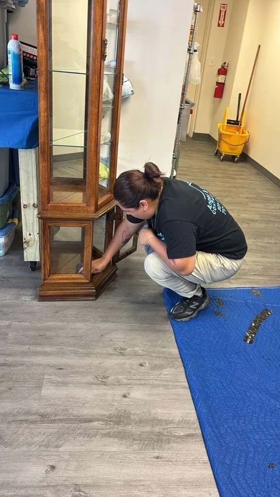 Crew member in a company shirt doing on-site contents cleaning of a wood display cabinet