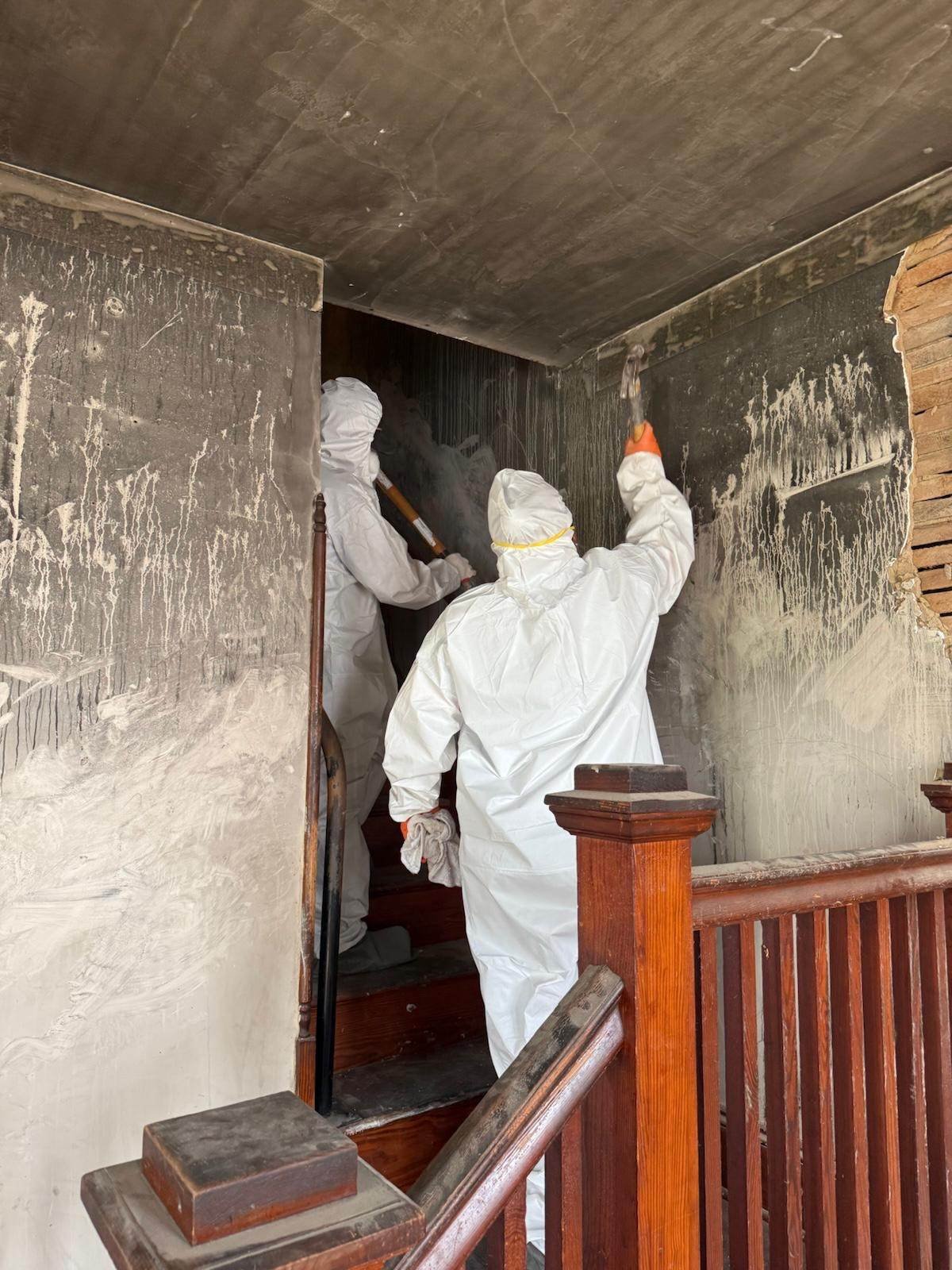 Crew members in protective suits cleaning fire-damaged walls on a staircase
