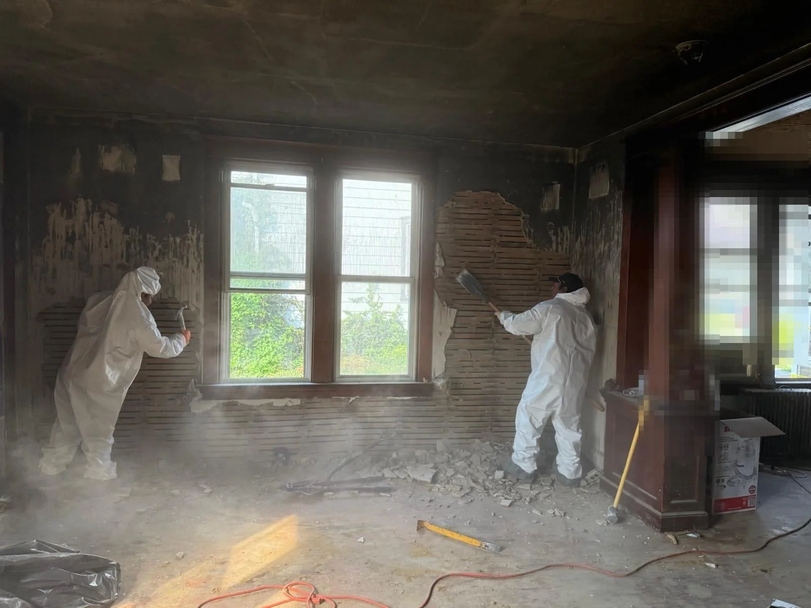 Crew members in protective suits demolishing fire-damaged plaster walls