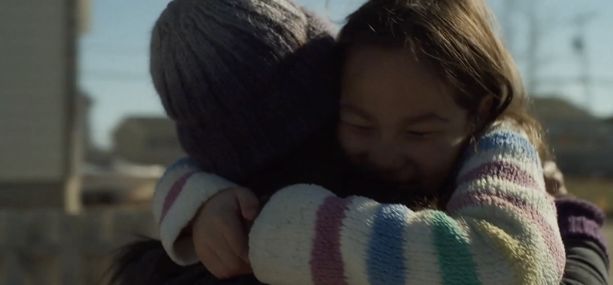 two young girls embrace, they are wearing warm winter sweaters and hats