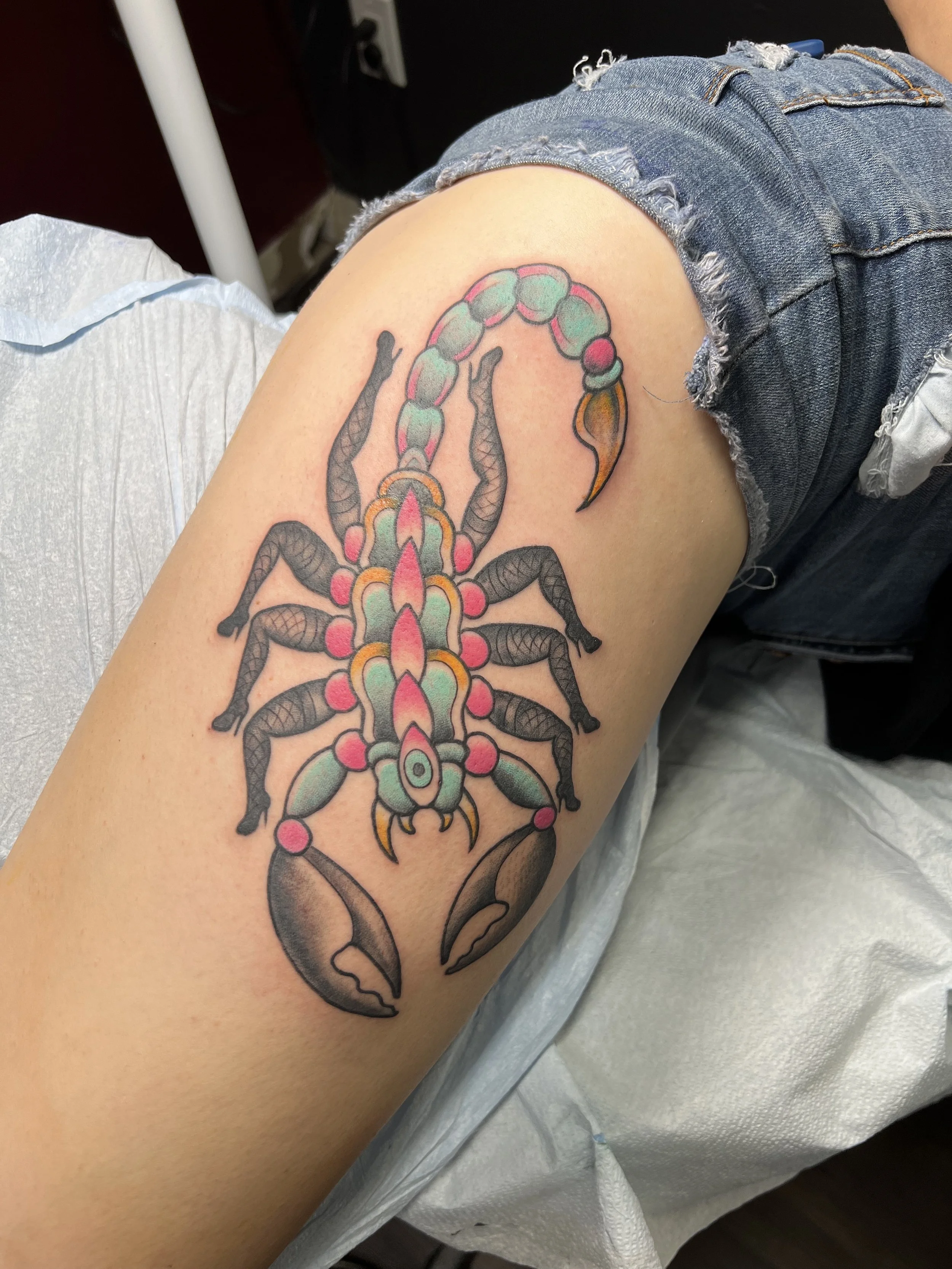 Colorful tattoo of a scorpion on a person's upper arm, featuring pink, green, and yellow details.