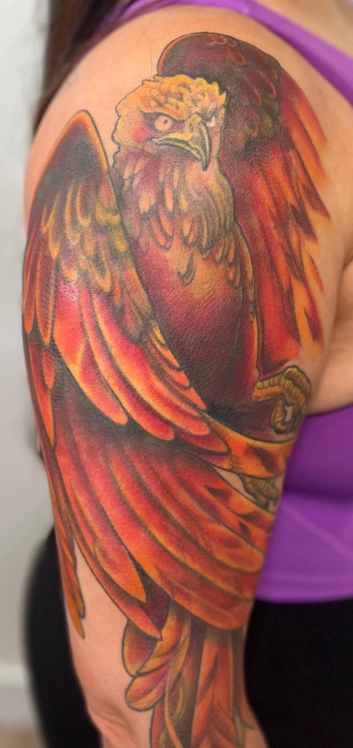 Tattoo of a red, orange, and yellow eagle with detailed feathers and sharp features on a person's upper arm.