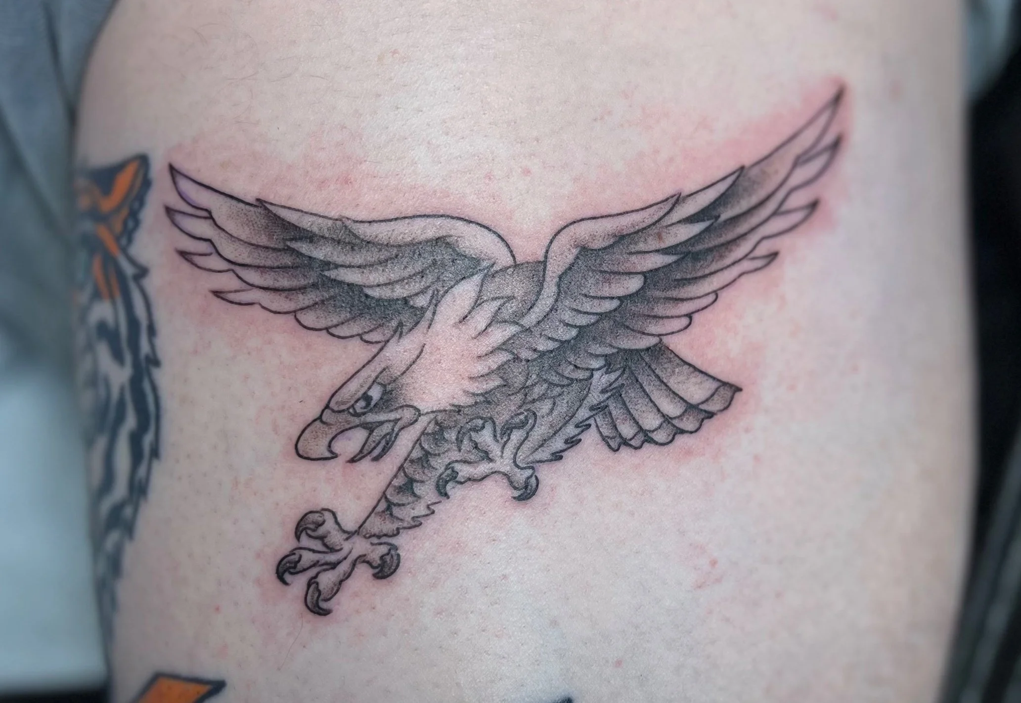 Black and gray tattoo of a flying eagle with a shield shape in its claws on a person's skin