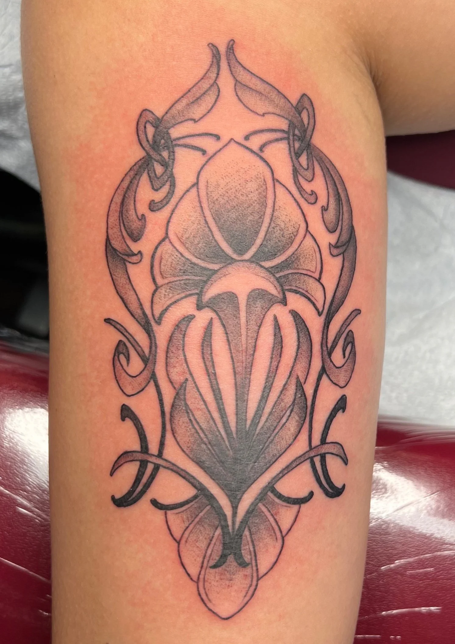 A tattoo on a person's thigh featuring a symmetrical, ornate design with floral and abstract elements, mostly in black ink.