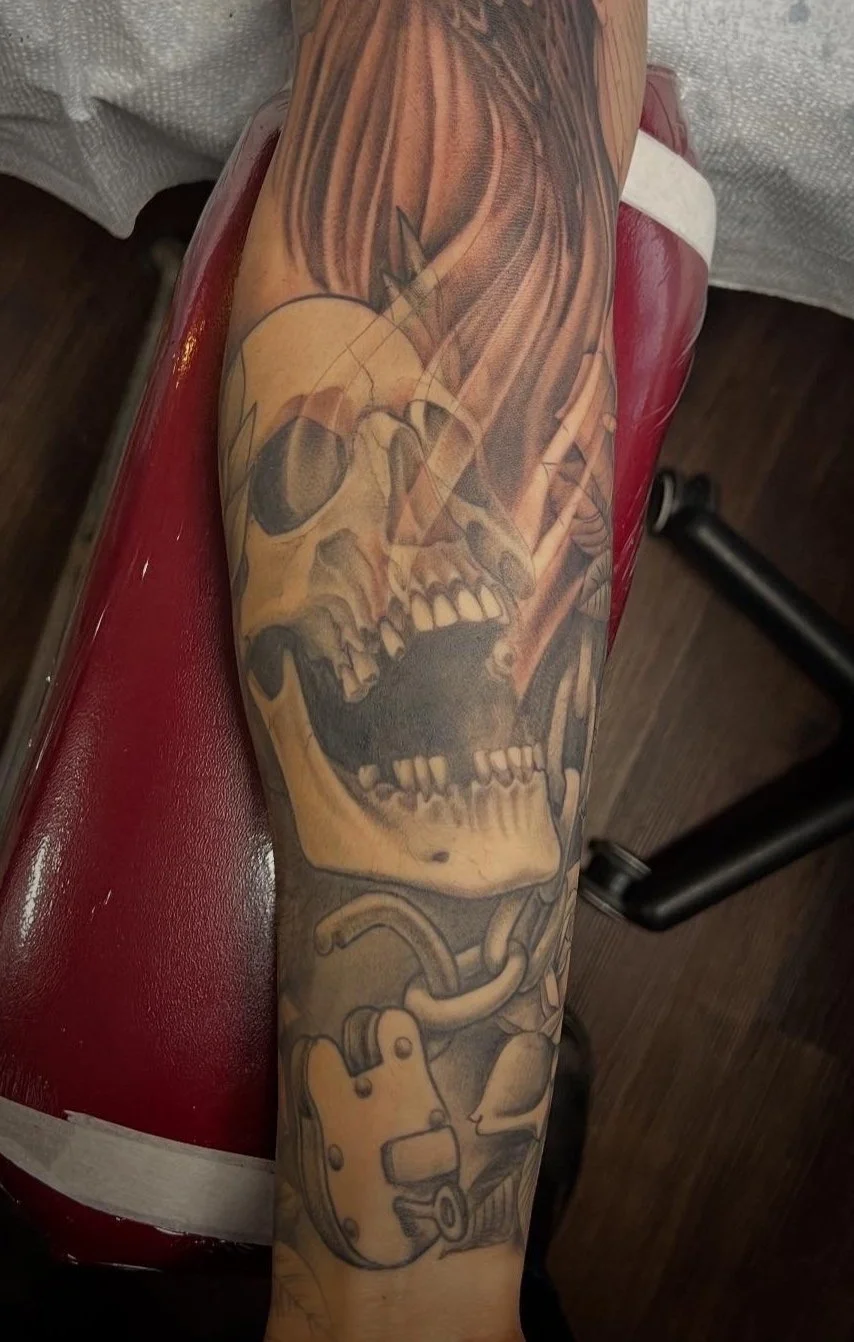 Tattoo of a phoenix rising from a skull with chains on a person's forearm.