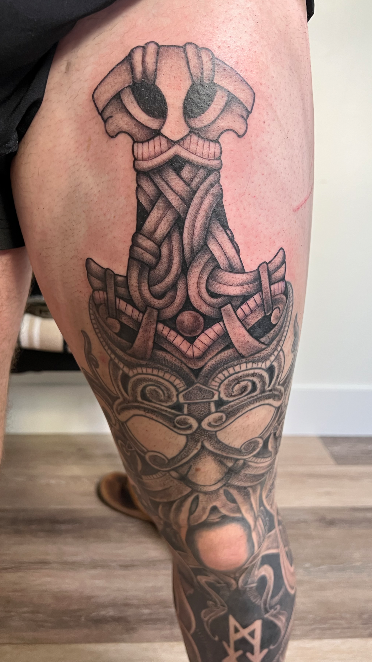 Detailed black and gray tattoo of a Viking ship with intricate knotwork and tribal designs on a person's thigh and leg.
