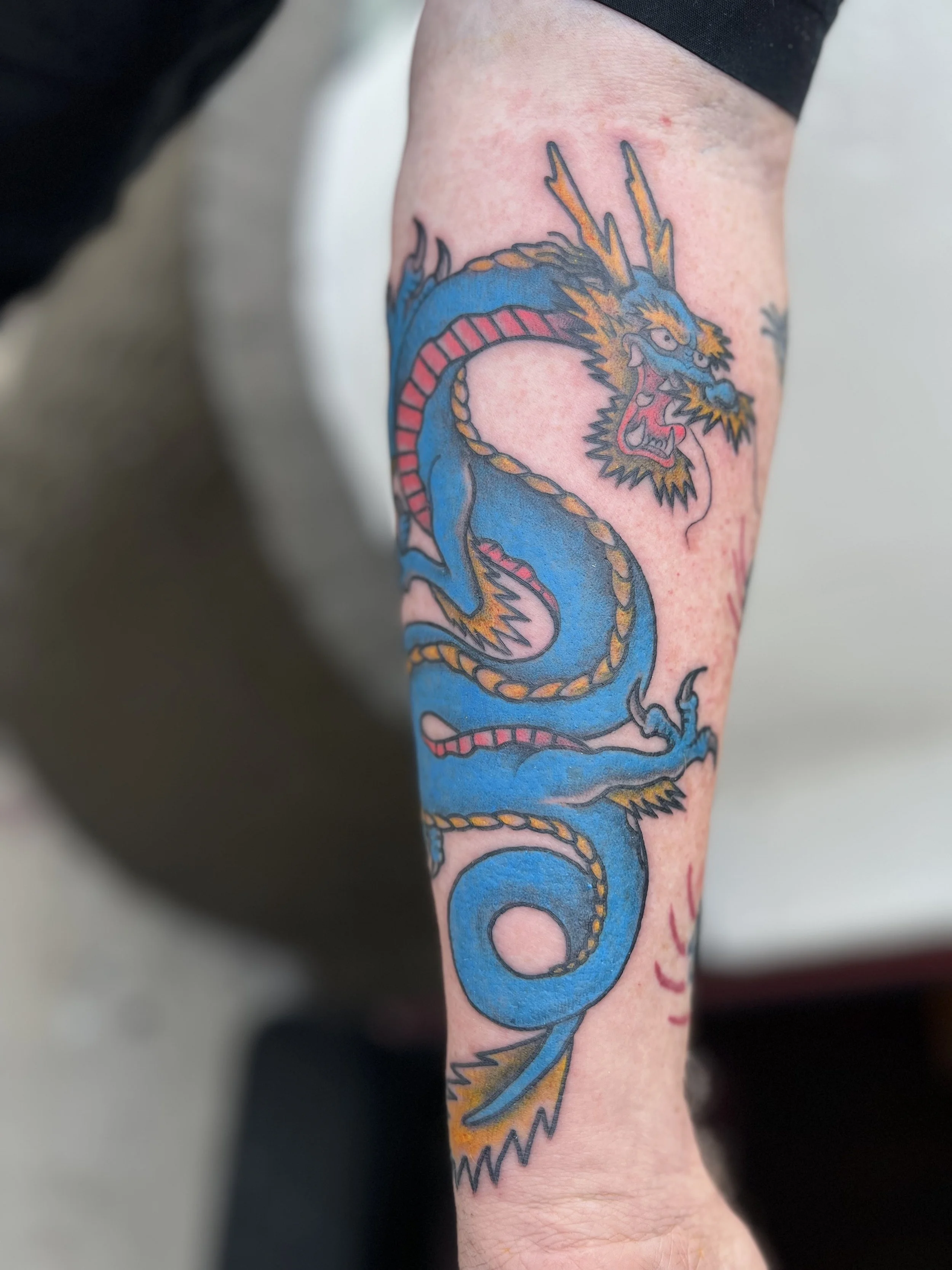 Colorful tattoo of a traditional-style blue and yellow Chinese dragon on a person's forearm.