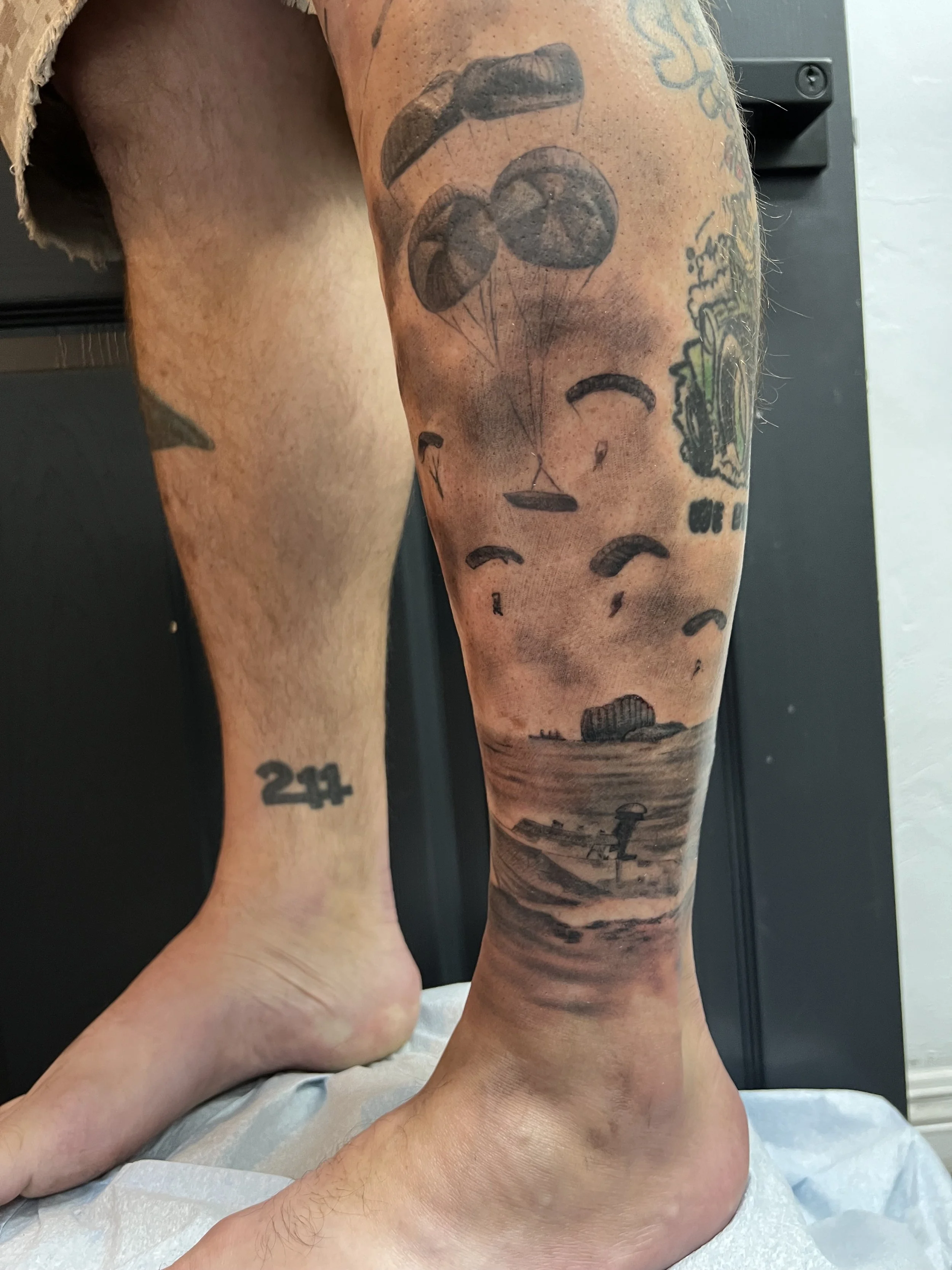 Tattoo of a beach scene with parachutes skydiving above and a lighthouse on the shoreline.