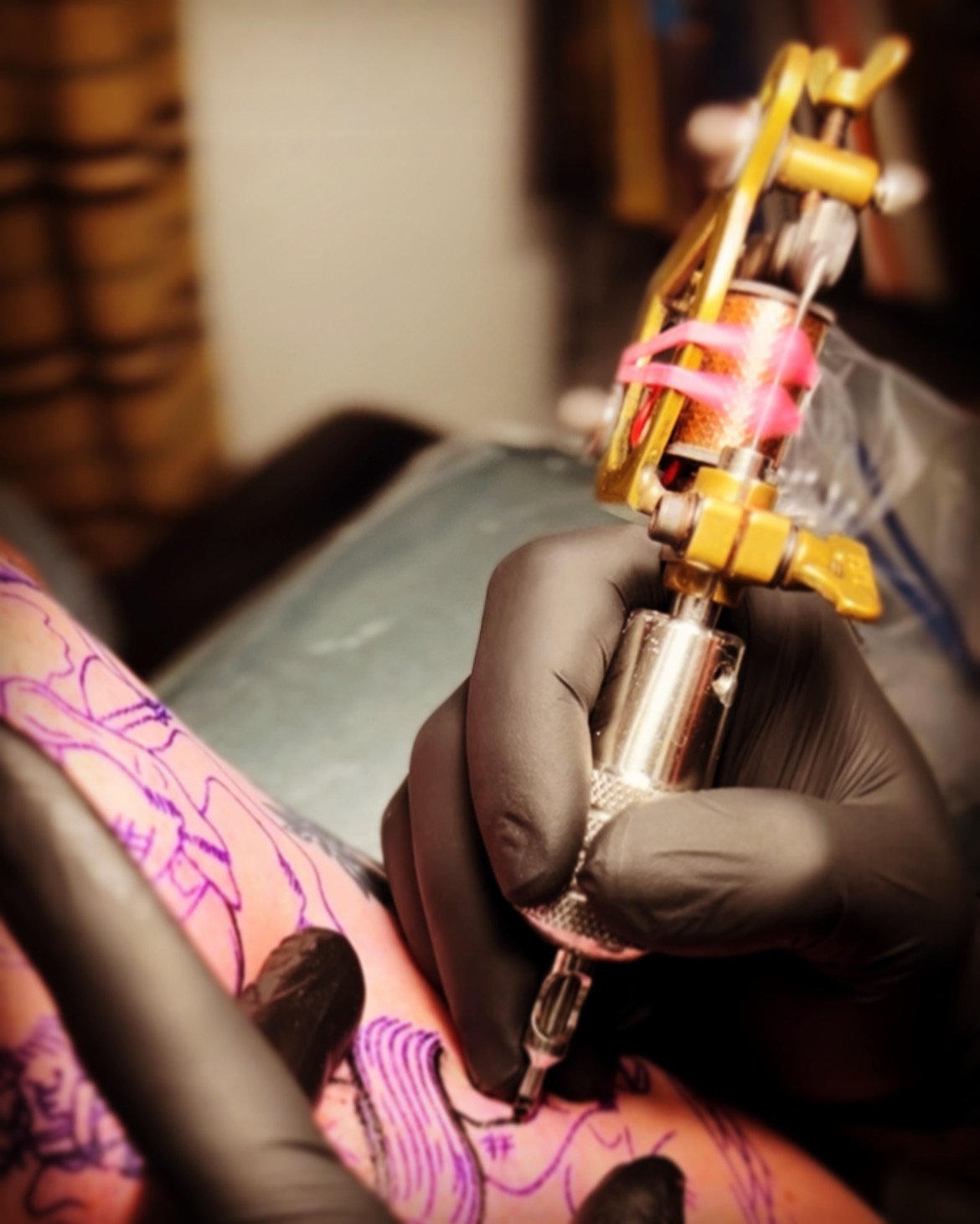 Close-up of a tattoo artist's hand with black gloves, holding a tattoo machine and tattooing a colorful design on a person's skin.