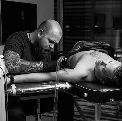 Tattoo artist working on a client's back in a tattoo studio, in black and white.