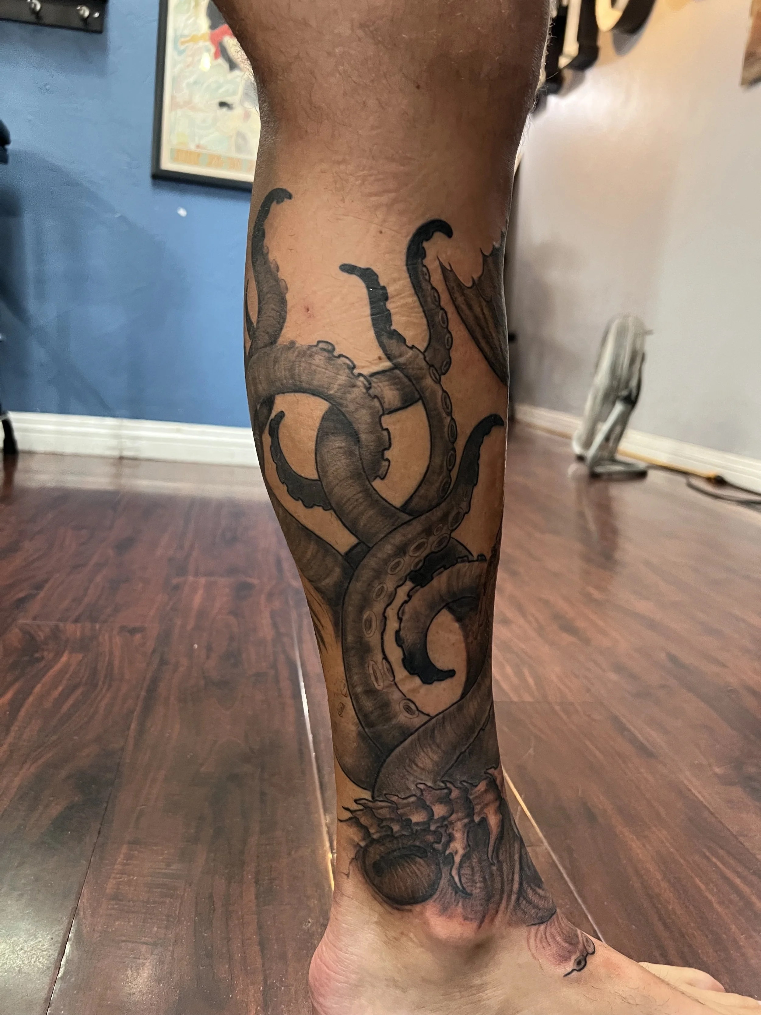 Tattoo of a detailed, black and gray octopus on a person's lower leg.