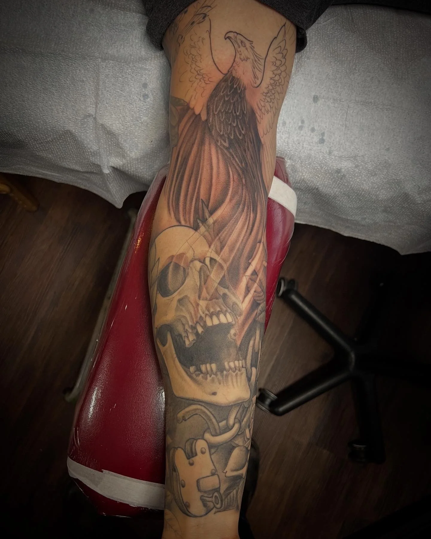 Tattoo of a phoenix rising from a skull with chains on a person's forearm.
