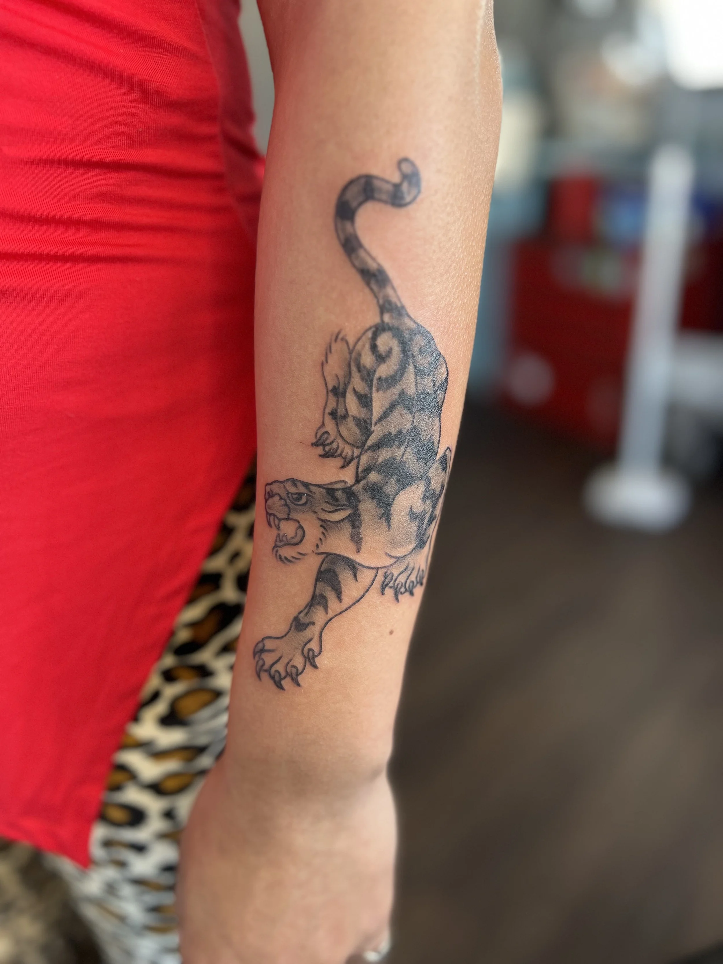 Tattoo of a roaring tiger on a person's forearm, with a signature below.