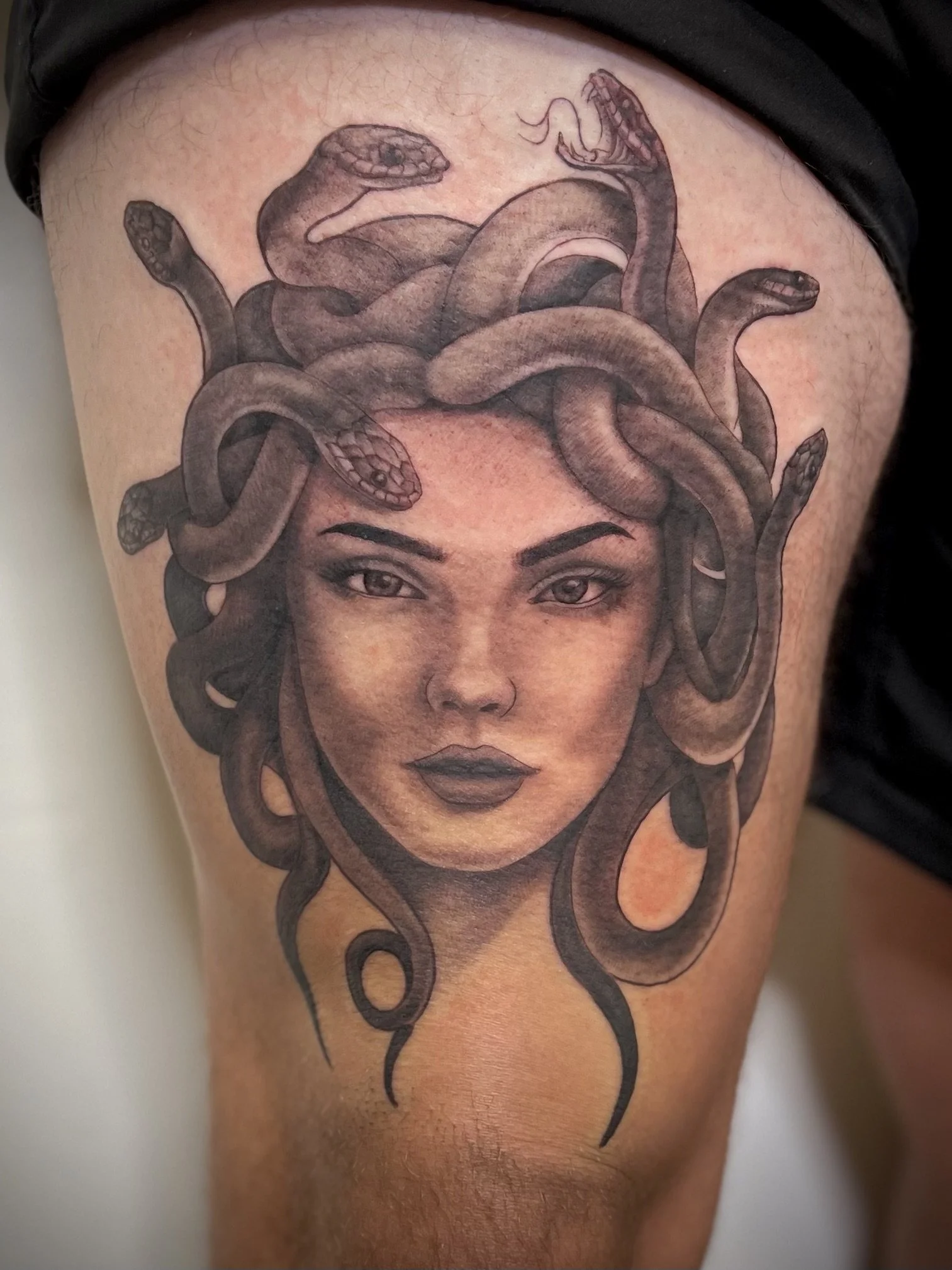 Tattoo of a woman's face with Medusa-like hair made of snakes on the thigh