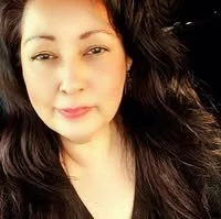 Close-up of a woman with long dark hair, wearing makeup, looking at the camera.