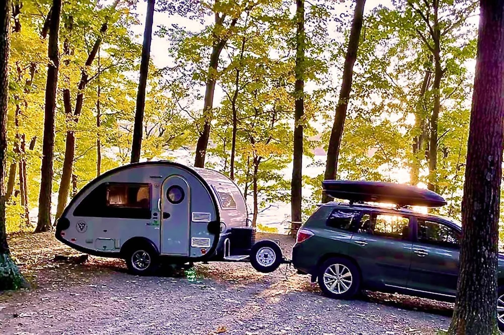 A car towing a teardrop camper through the woods at sunset