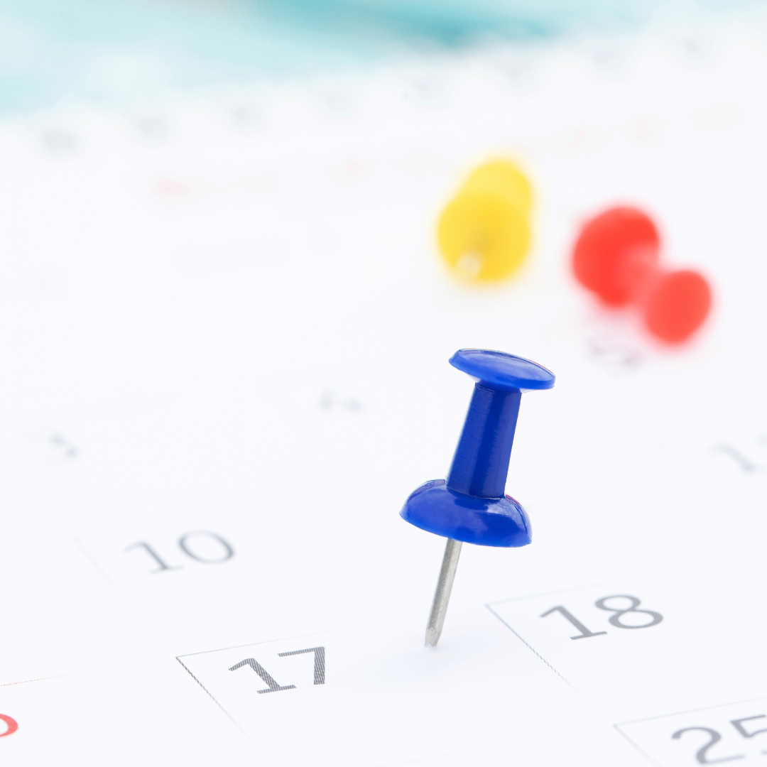 A blue push pin marking the 17th on a calendar with blurred yellow and red balloons in the background.