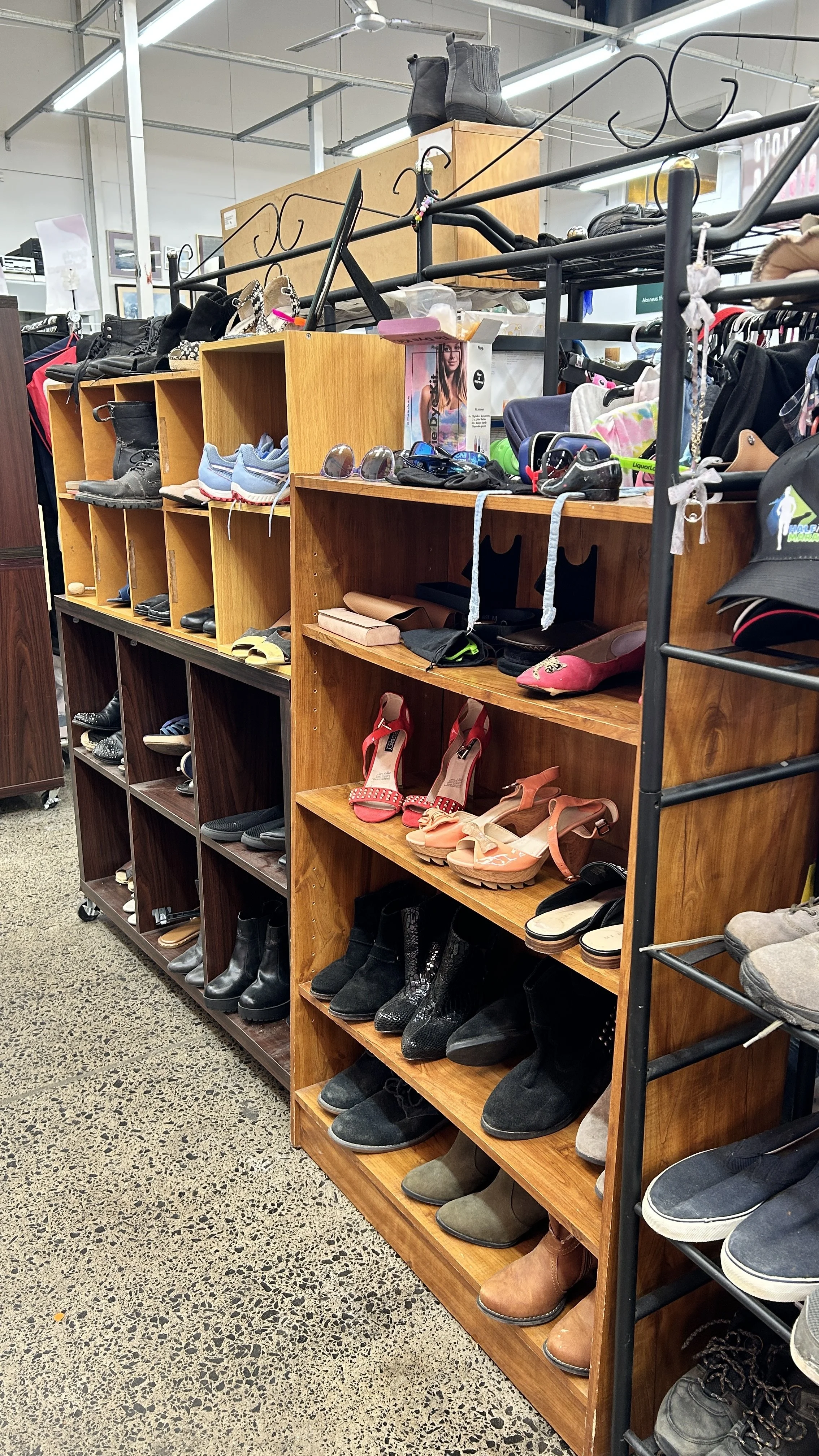 A display of various shoes including boots, sandals, and sneakers on wooden shelves in a thrift store.