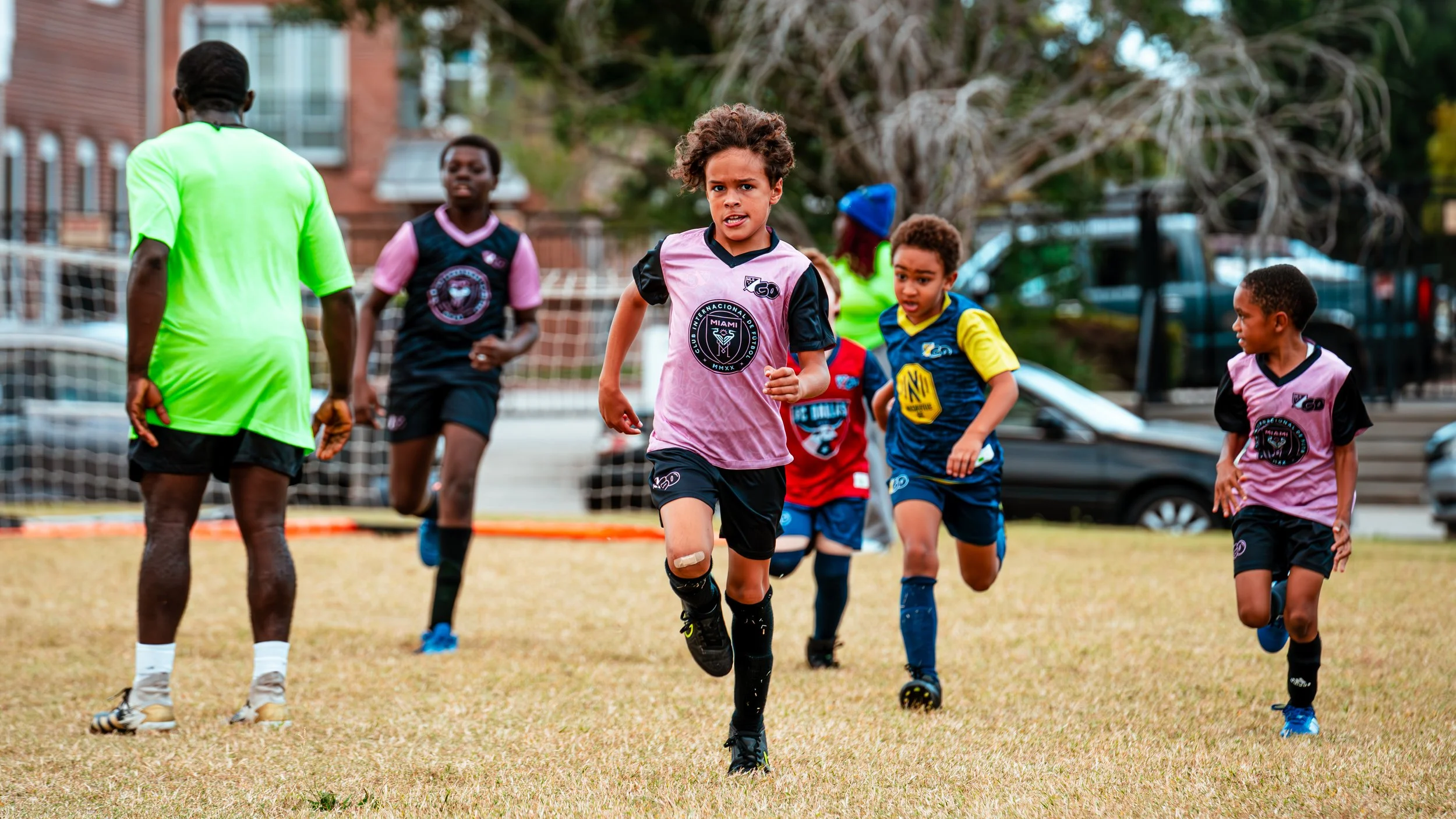 Children playing soccer on a grassy field, running towards the camera, with a referee visible.