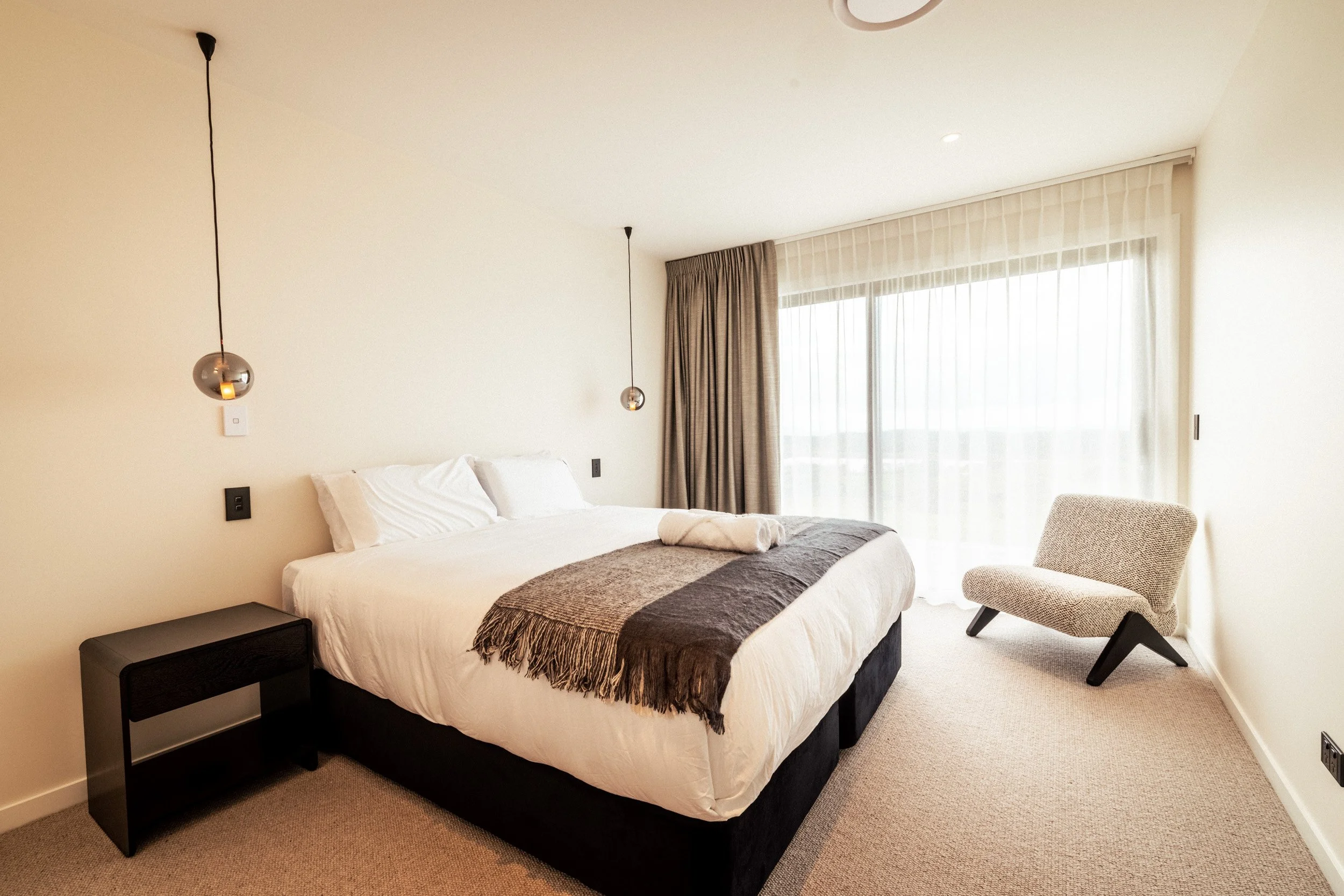 Guest bedroom at Ocean View Te Arai with sliding door opening to a private deck and panoramic views of the Pacific Ocean, lakes, pine forest, and farmland, featuring a super king bed, premium bedding, and luxury finishes.