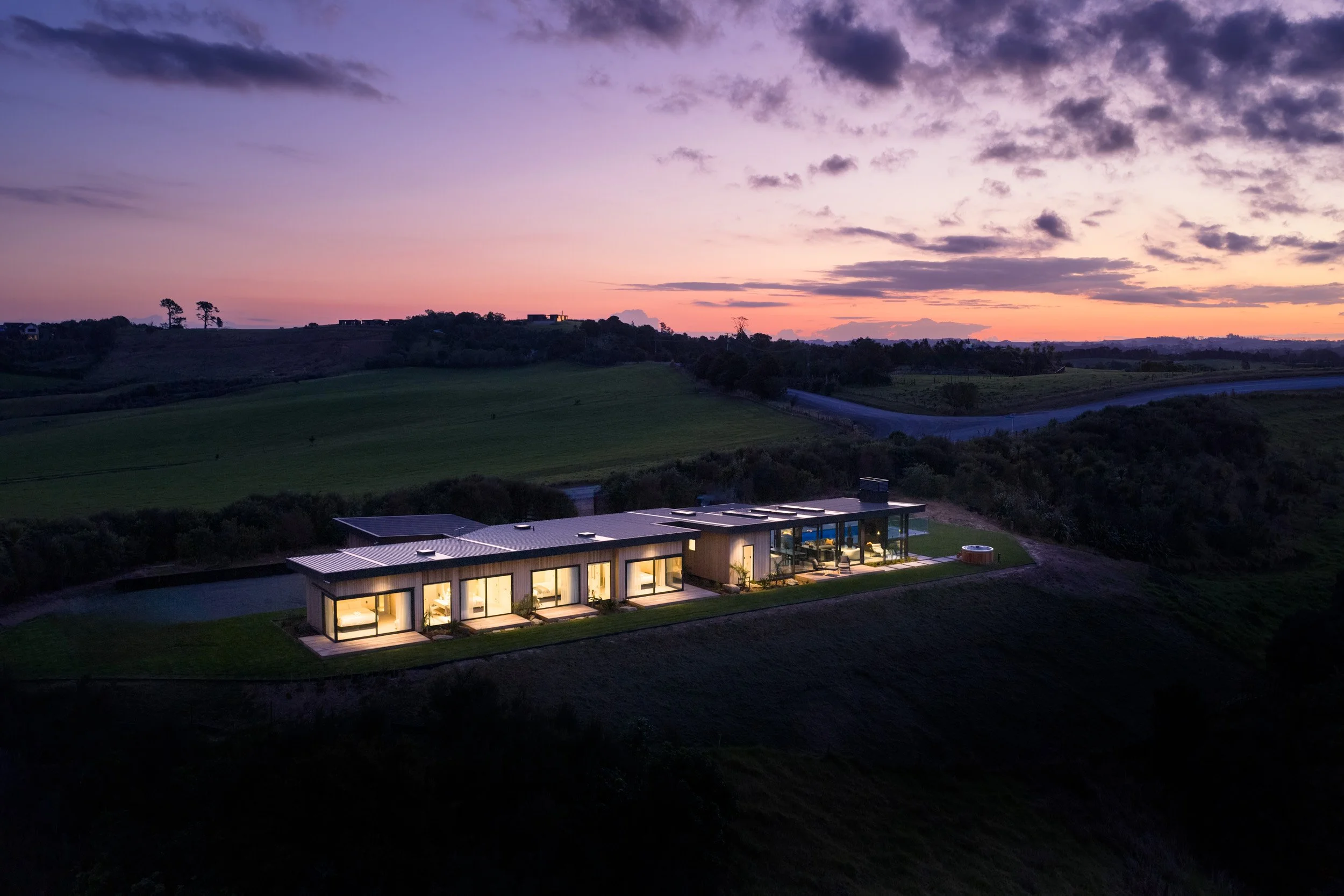 Twilight exterior of Ocean View Te Arai showcasing seaward-facing decks, feature lighting, with an illuminated swimming pool and spa.