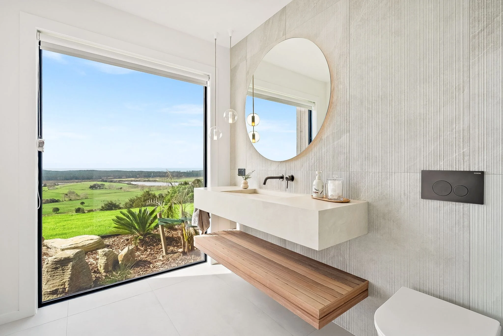 One of the master bathroom at Ocean View Te Arai featuring a walk-in shower with floor-to-ceiling tiles, a bespoke ramp sink vanity, underfloor heating and a full-length window framing breathtaking coastal views.