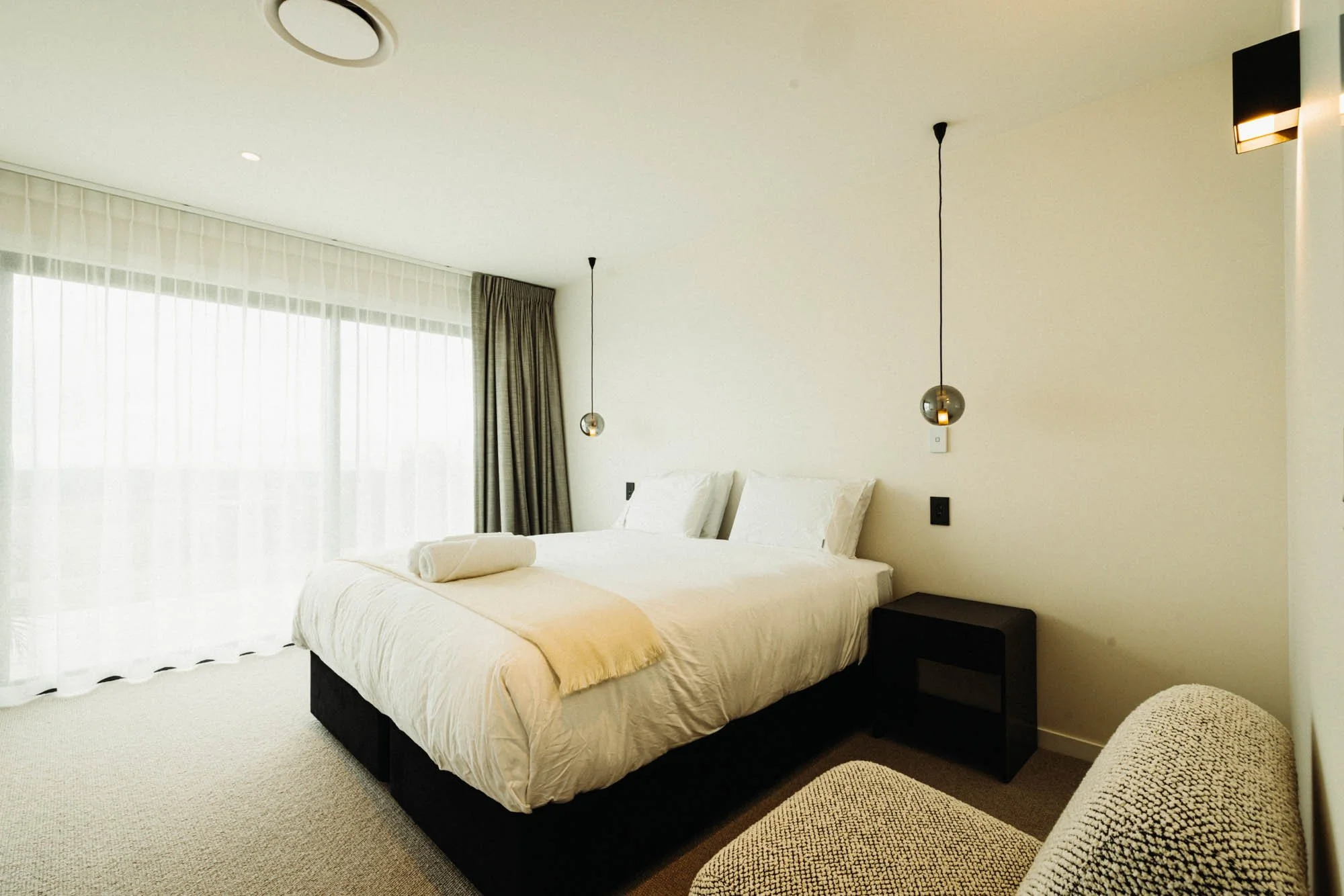 One of the guest bedrooms at Ocean View Te Arai, featuring a super king bed with premium bedding and luxury finishes, and a sliding door that opens to a private deck with sweeping views of the Pacific Ocean, lakes, pine forest, and surrounding farmla