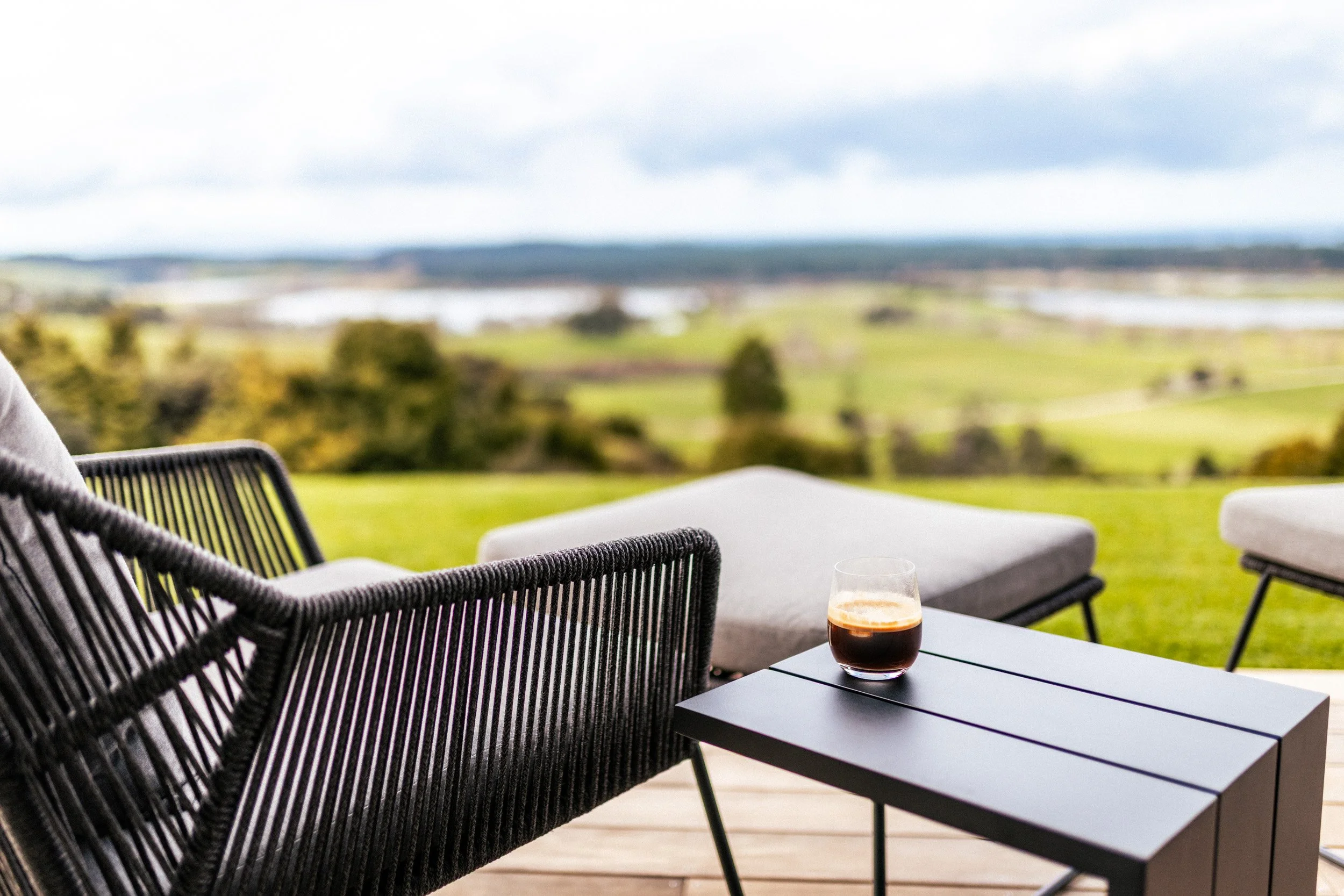 Outdoor lounge chairs and footstools on the deck at Ocean View Te Arai, perfect for enjoying coffee with panoramic views of the Pacific Ocean, Hen and Chickens Islands, lakes, and Te Arai Links pine forests.