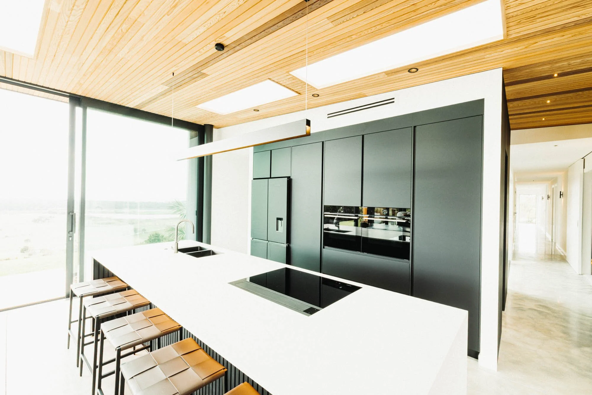 Designer kitchen at Ocean View Te Arai featuring a concrete island, state-of-the-art appliances including Gaggenau cooktop, skylights and wrap-around coastal views through floor-to-ceiling glass which slide to give indoor-outdoor flow.