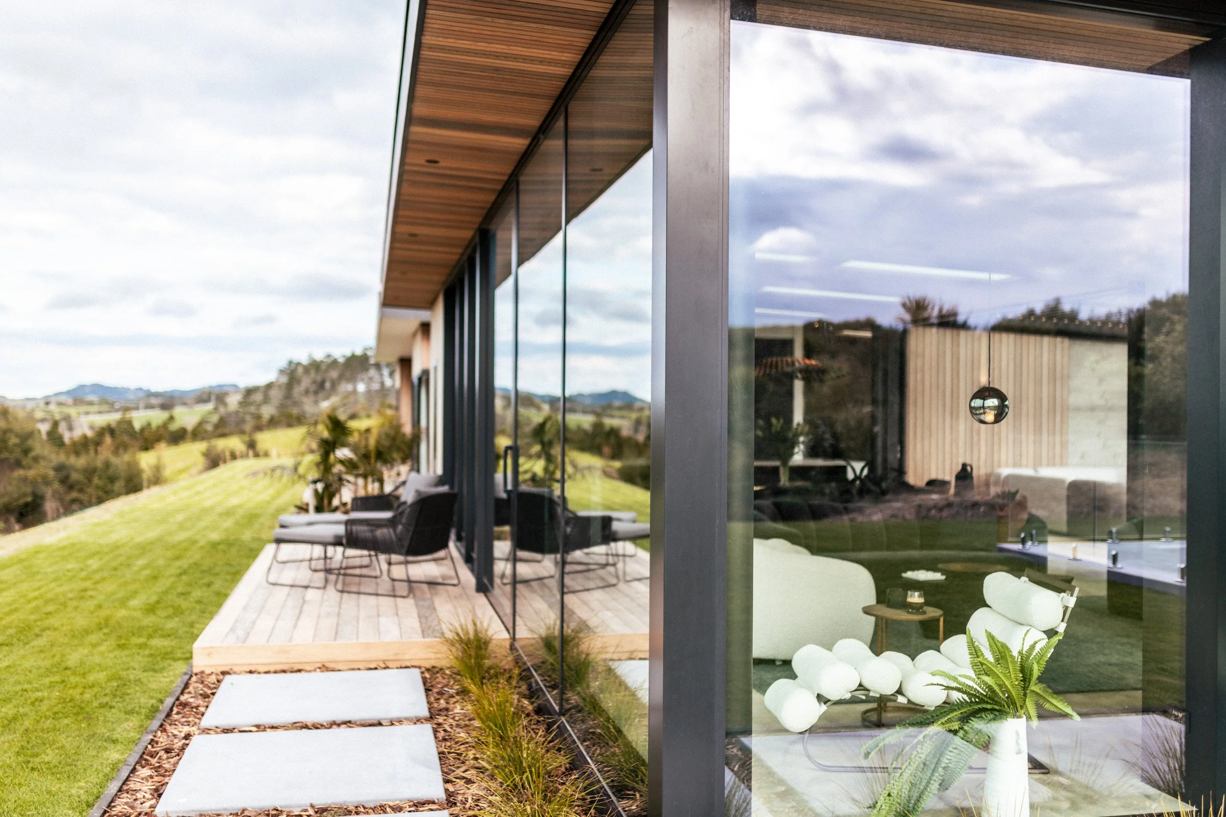 Floor-to-ceiling glass in the living area at Ocean View Te Arai, opening to sun-drenched decks and wrap-around lawn that maximises panoramic coastal views.