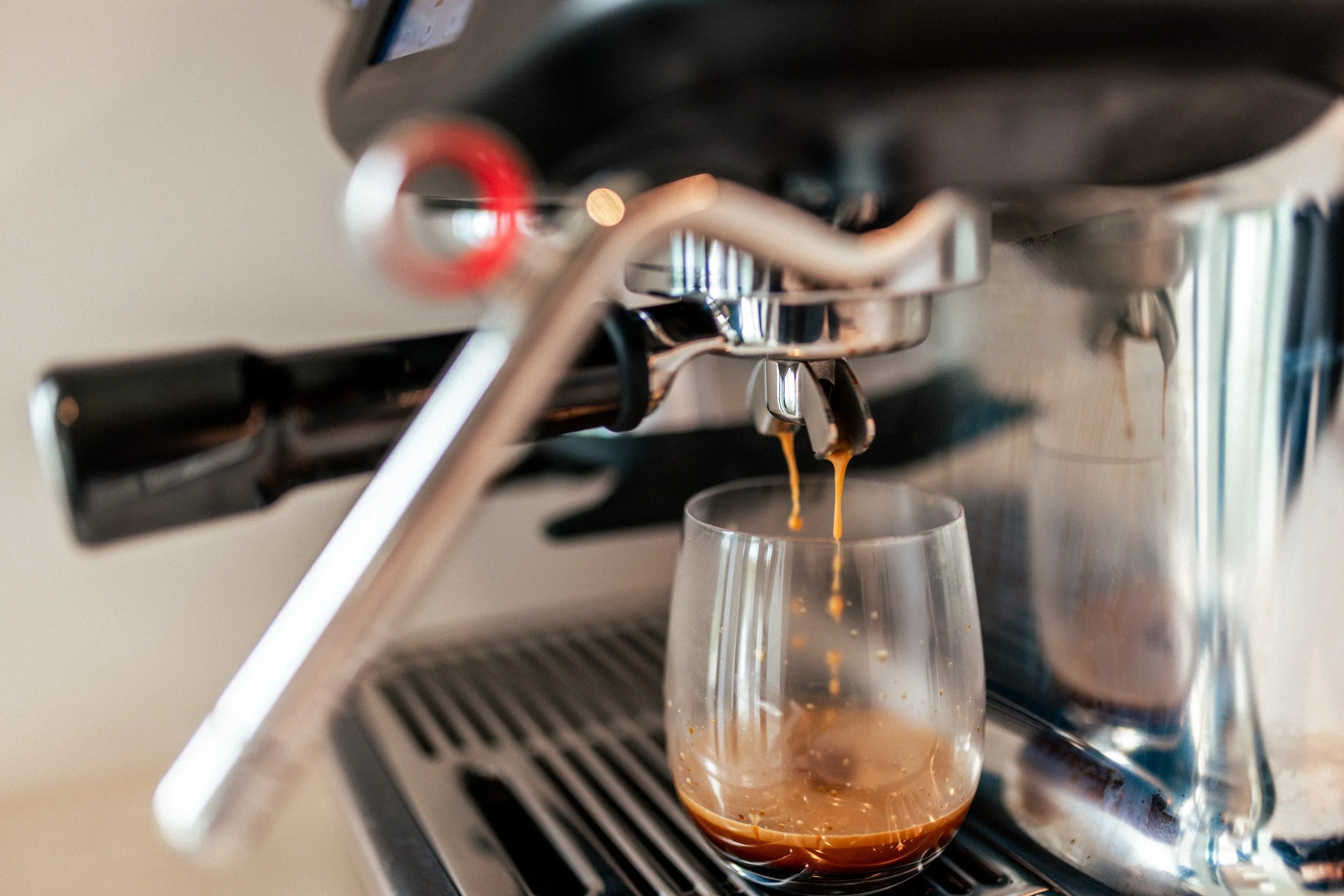 Close-up of the state-of-the-art coffee machine in the scullery at Ocean View Te Arai, with views through the full-length window across the landscape while making a morning coffee.