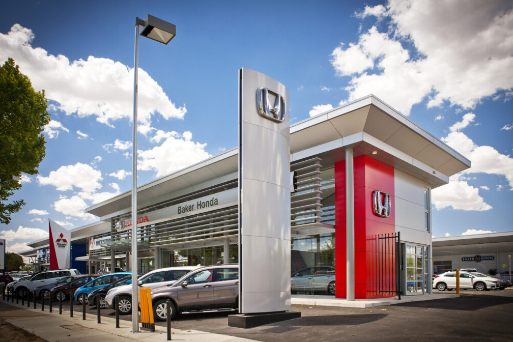 Exterior view of Honda car dealership with brand signage and parked cars outside on a sunny day.