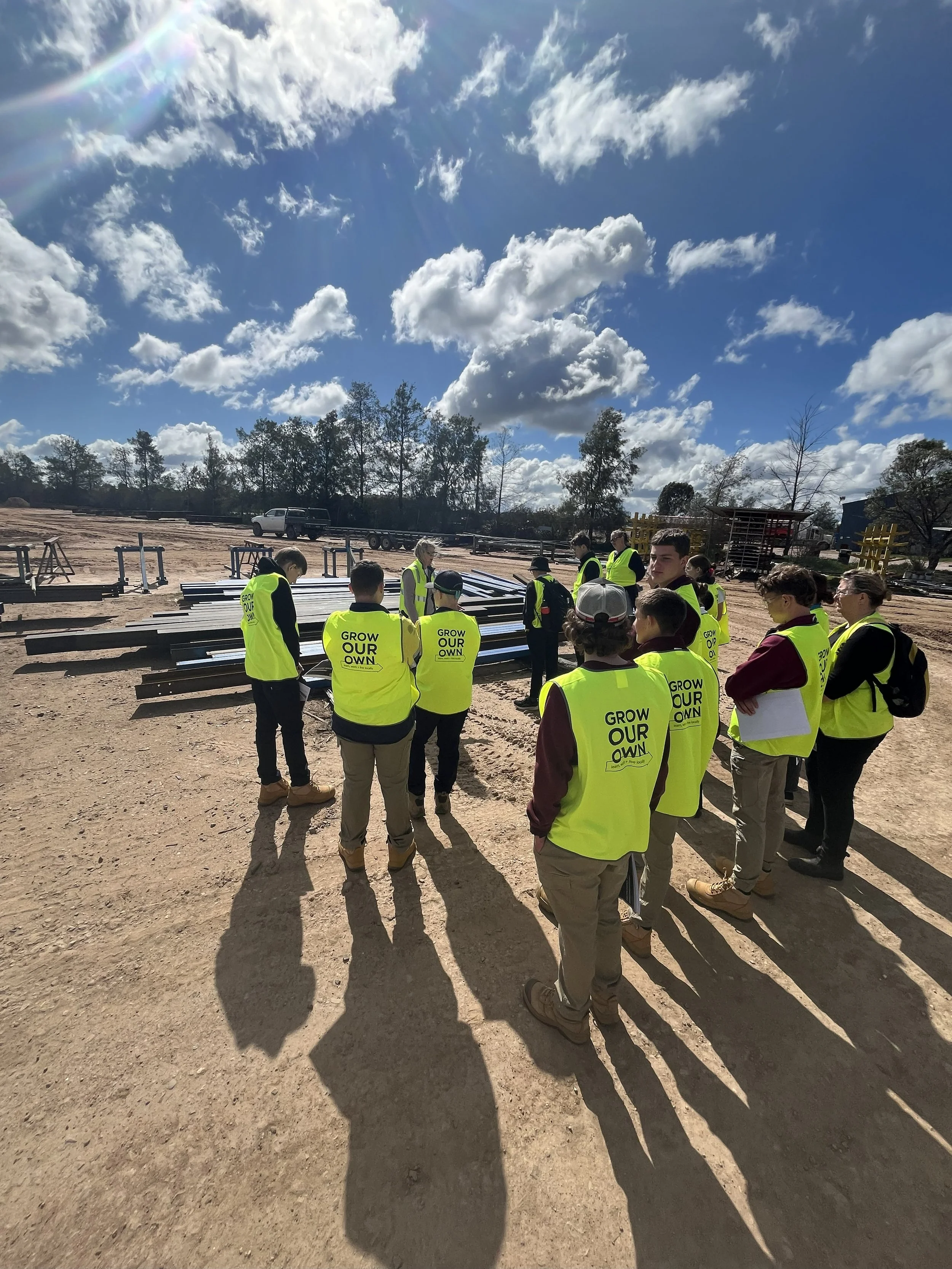 Group of students on an Industry tour of Hutchins Bros, wearing yellow safety vests gathered looking at steel in Hutchins Bros yard.