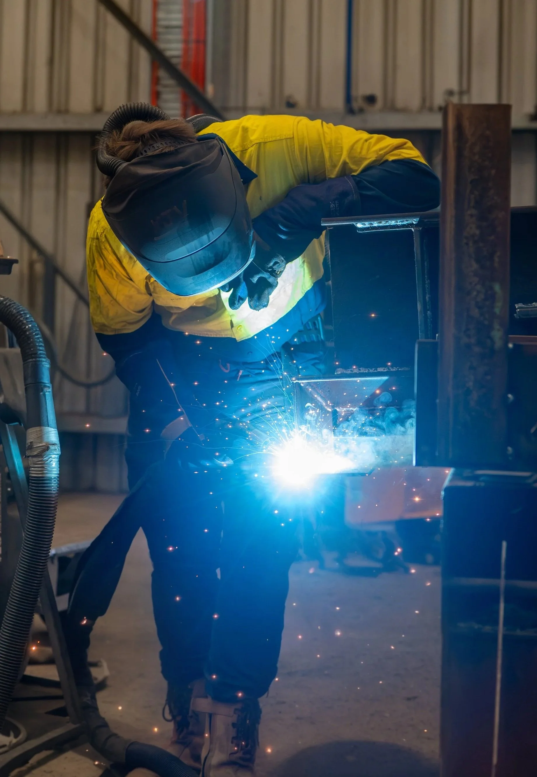 A tradesman wearing a welding helmet and PPE welding a beam in the Hutchins Bros workshop.