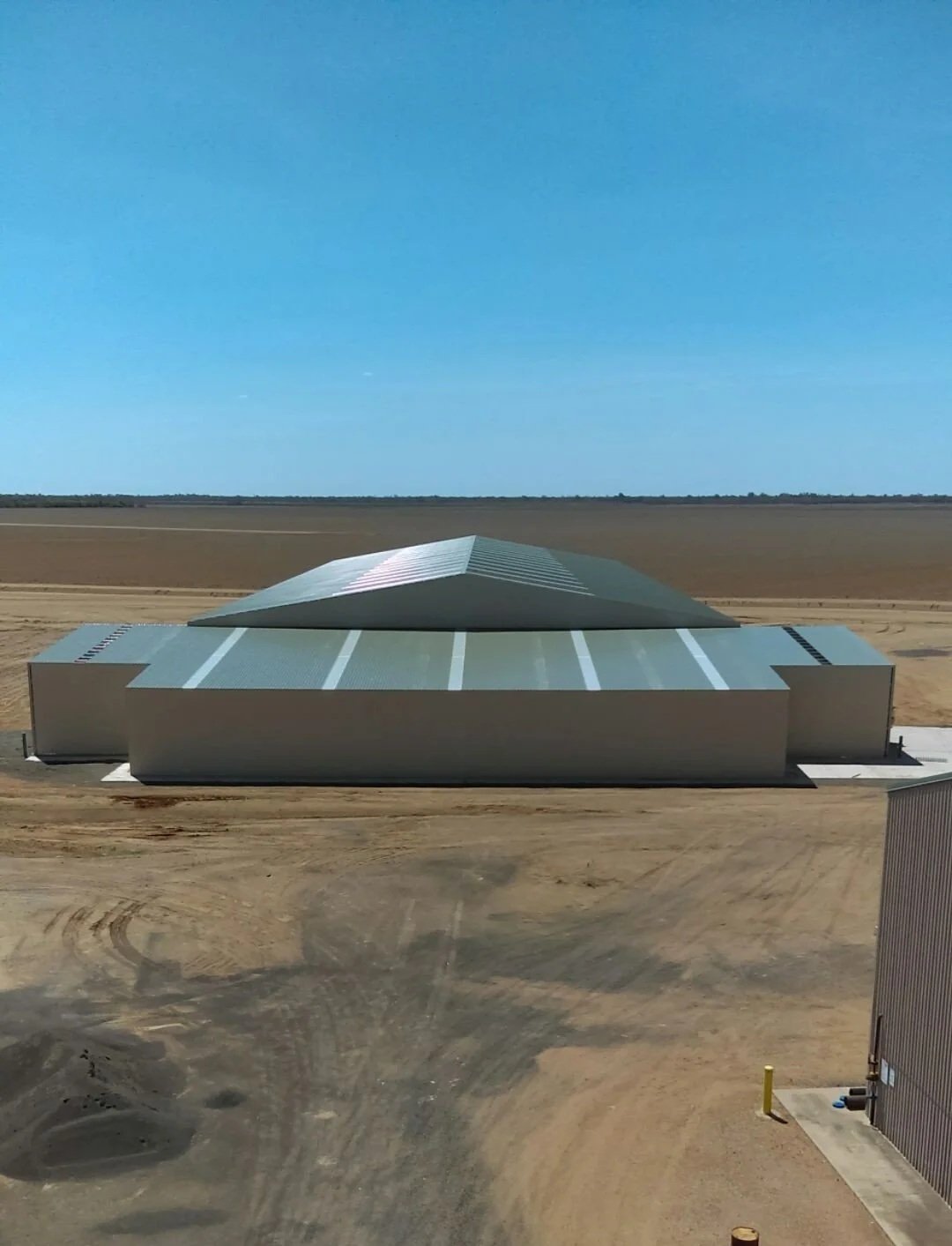 Large industrial or military building with a sloped roof, situated in a barren, flat landscape under a clear blue sky.