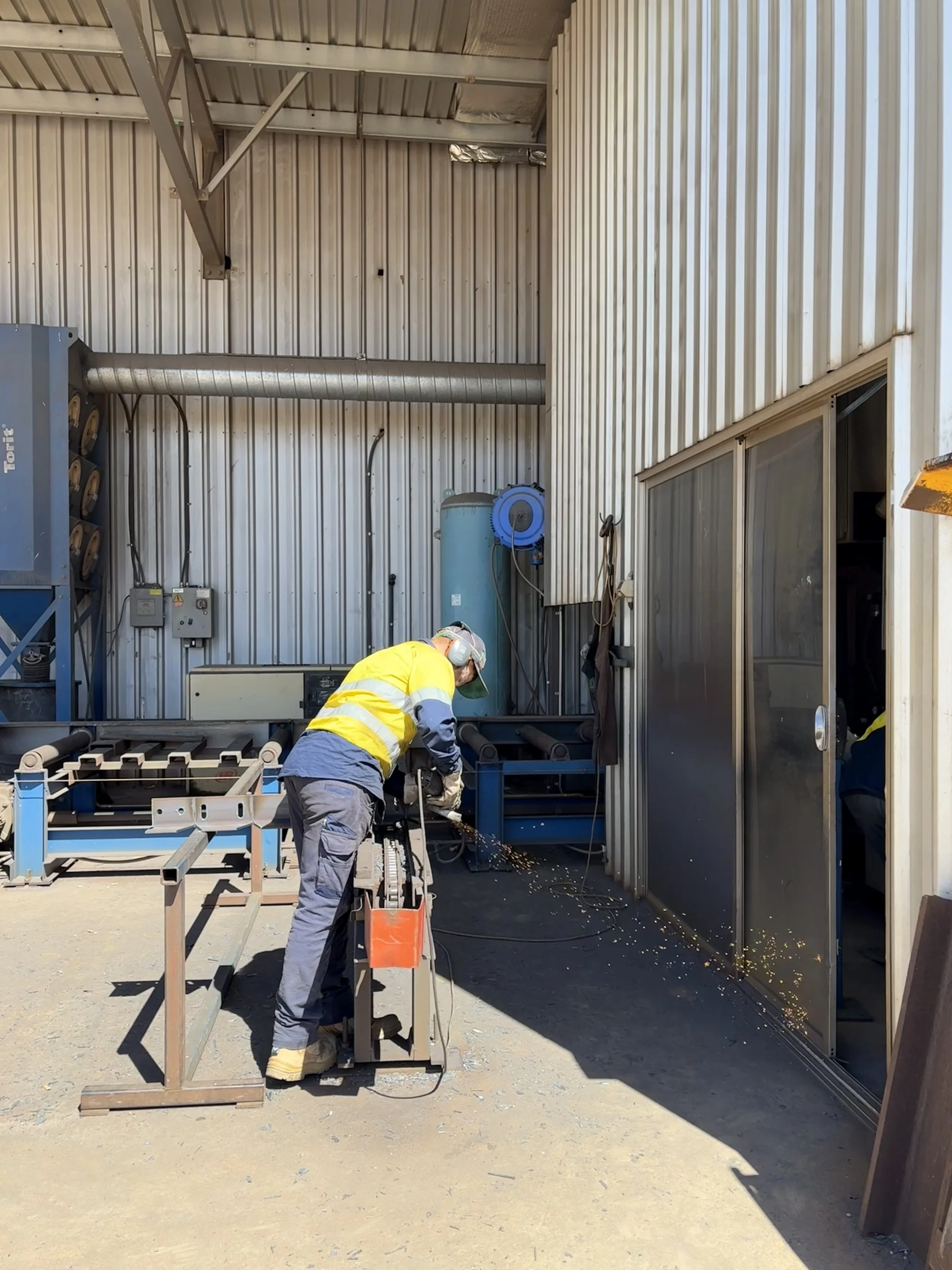 Out near the beamline, a work experience student, is using an angle grinder to smooth the edge of a steel beam.