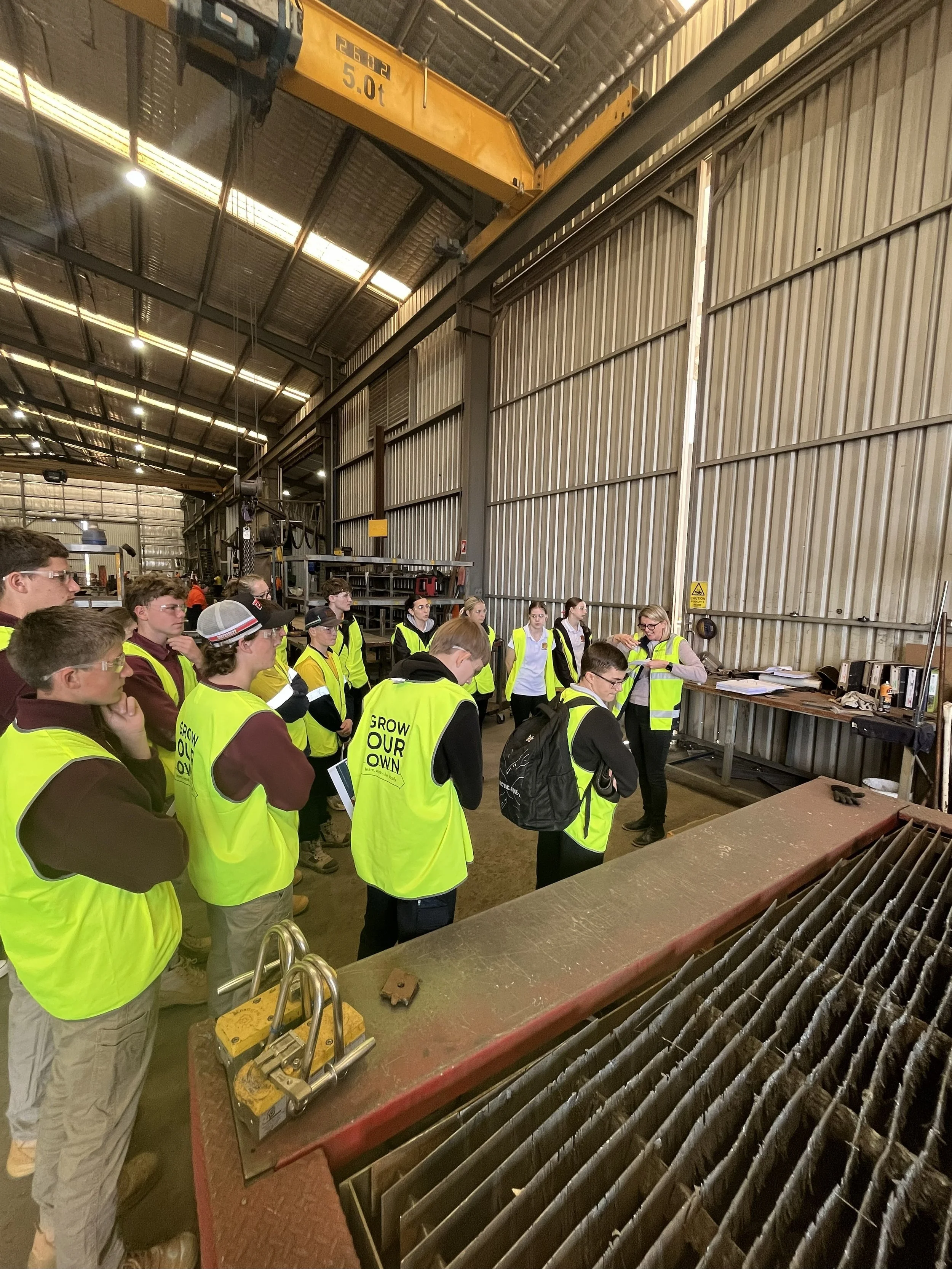 Gathered in the workshop, a group of students on an Industry tour of Hutchins Bros, listening to Hutchins Bros director explain about the operations of the workshop.