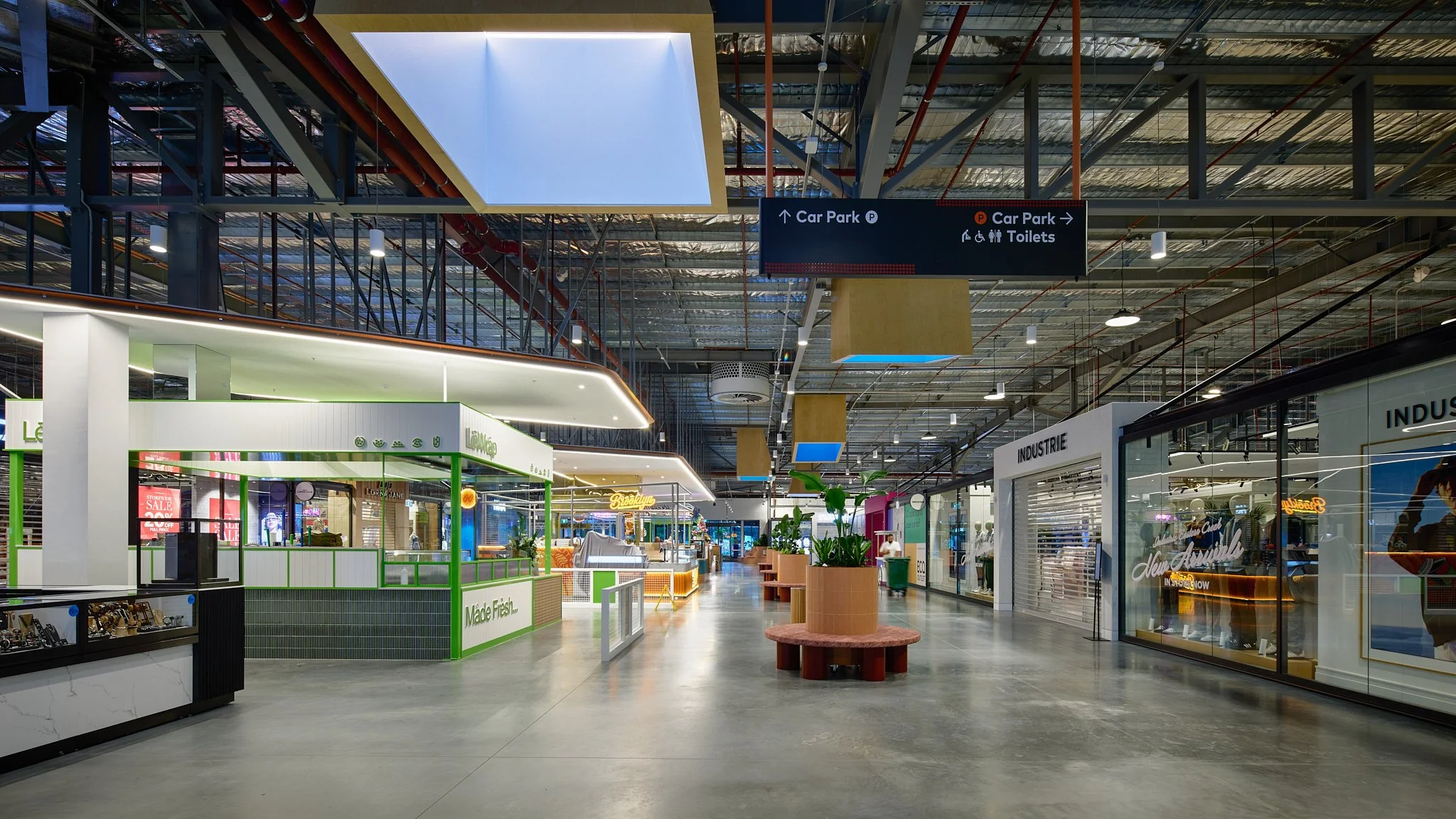 Interior of a shopping mall with stores, a seating area, and a sign indicating directions to car park and toilets.