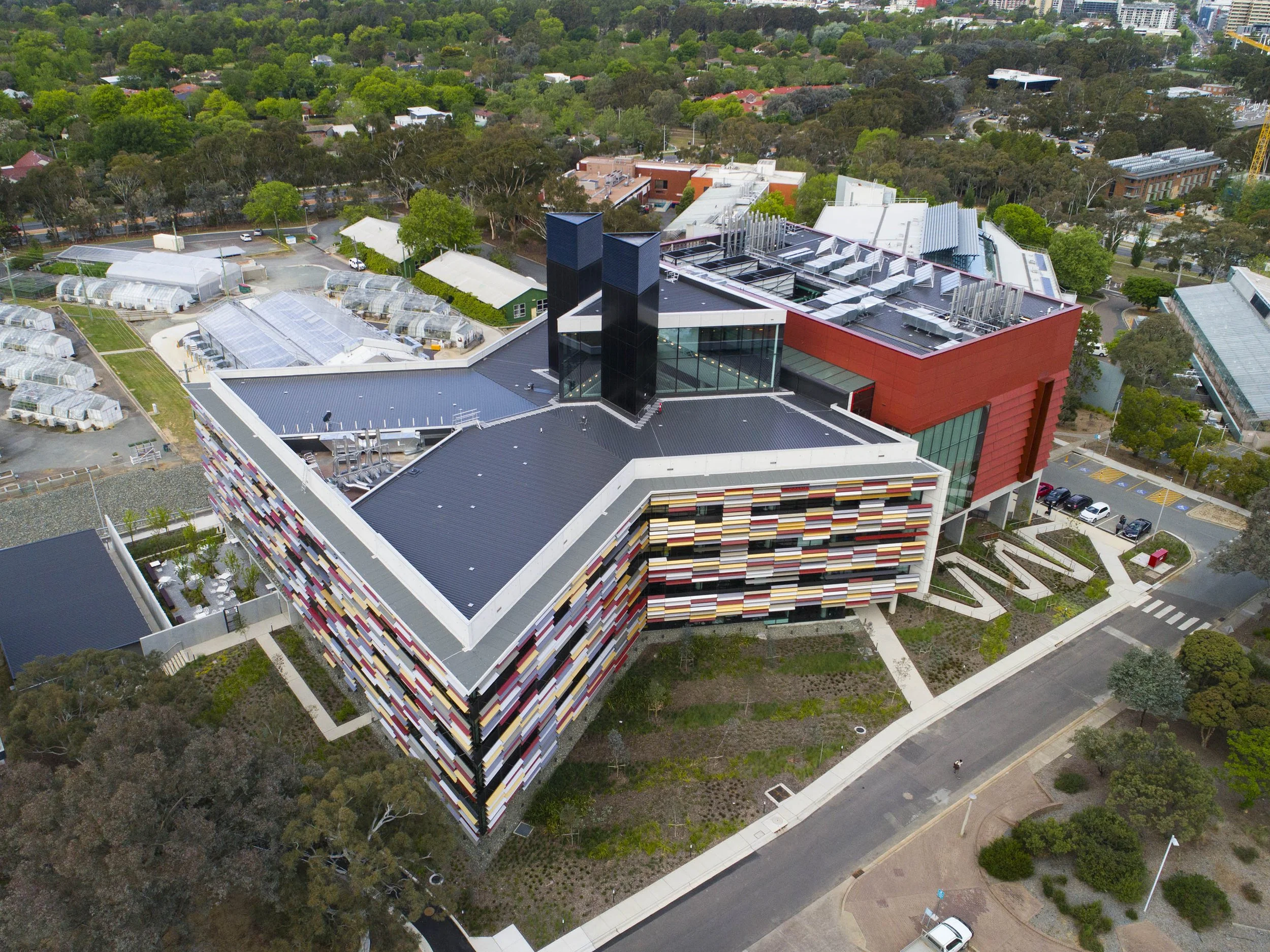 Aerial view of a modern building with colorful facade, surrounded by green trees and parking lot, with a residential neighborhood in the background.