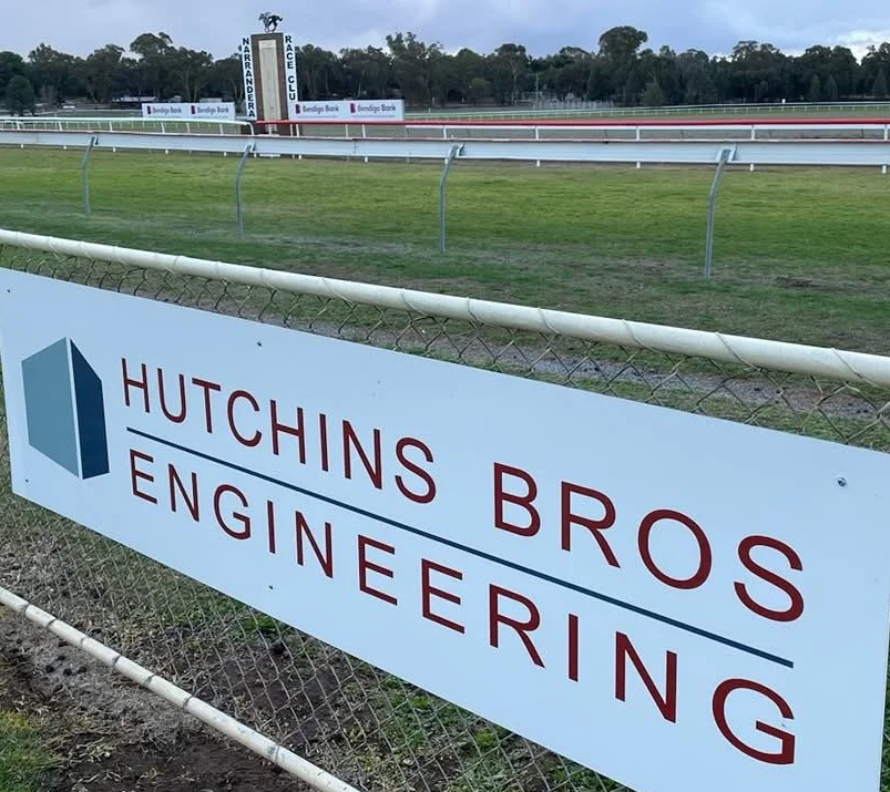 View of a racetrack with a sign for Hutchins Bros Engineering in the foreground.