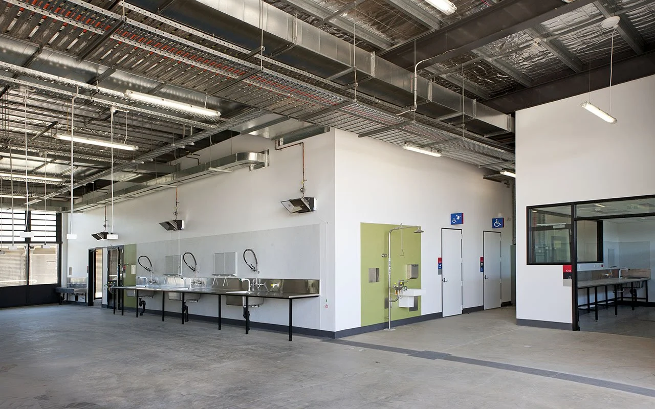 An unfinished commercial restroom or wash area with sinks, faucets, and a water fountain, featuring accessible signs and doors.