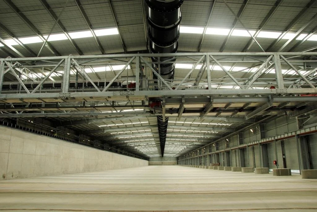 Empty industrial warehouse with a large overhead pipe and metal framework on the ceiling.