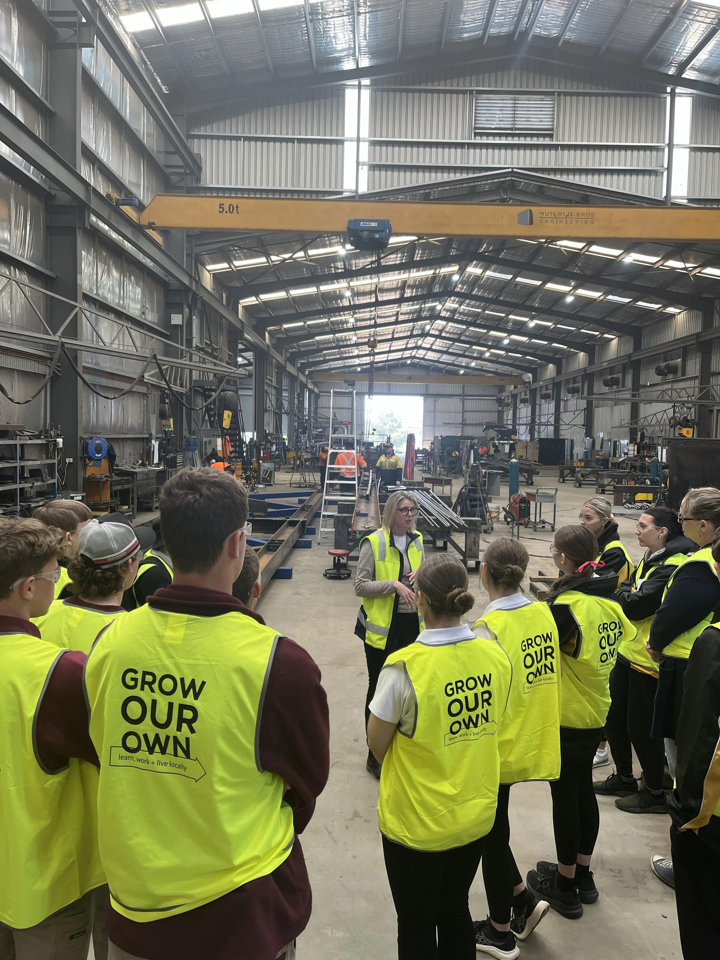 Gathered in the workshop, a group of students on an Industry tour of Hutchins Bros, listening to Hutchins Bros director explain about the operations of the workshop.