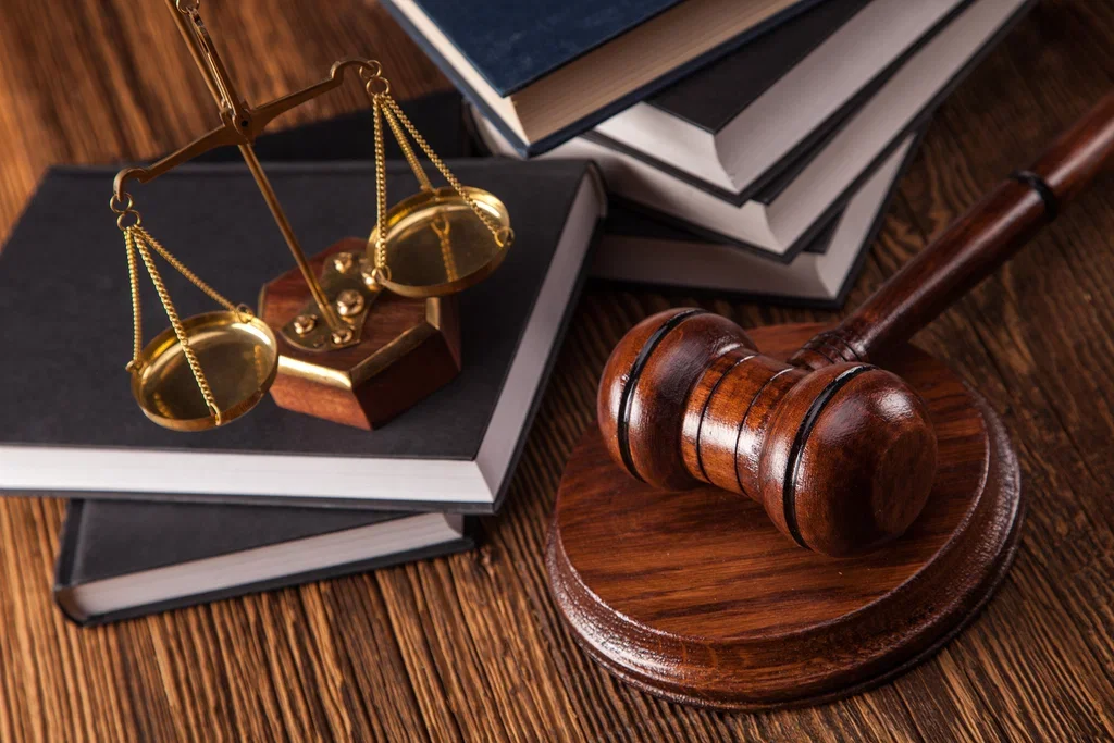 A wooden gavel, a set of scales of justice, and a stack of legal books on a wooden surface.