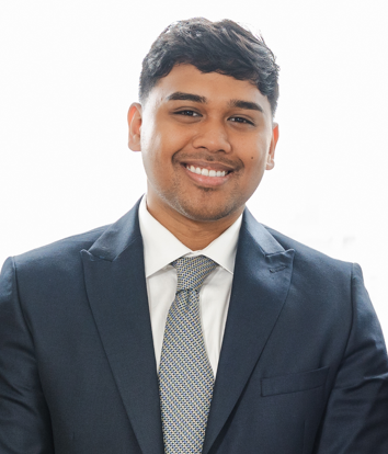 Portrait of a young man in a dark suit and tie smiling at the camera against a plain white background.