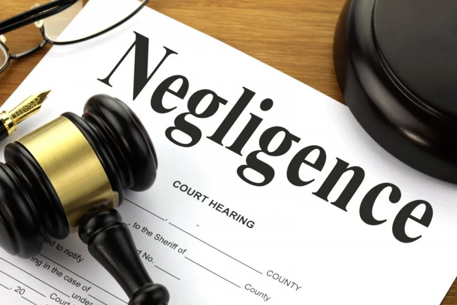 A legislative document titled 'Negligence' with a gavel resting on top of it, a pen, and eyeglasses on a wooden surface.